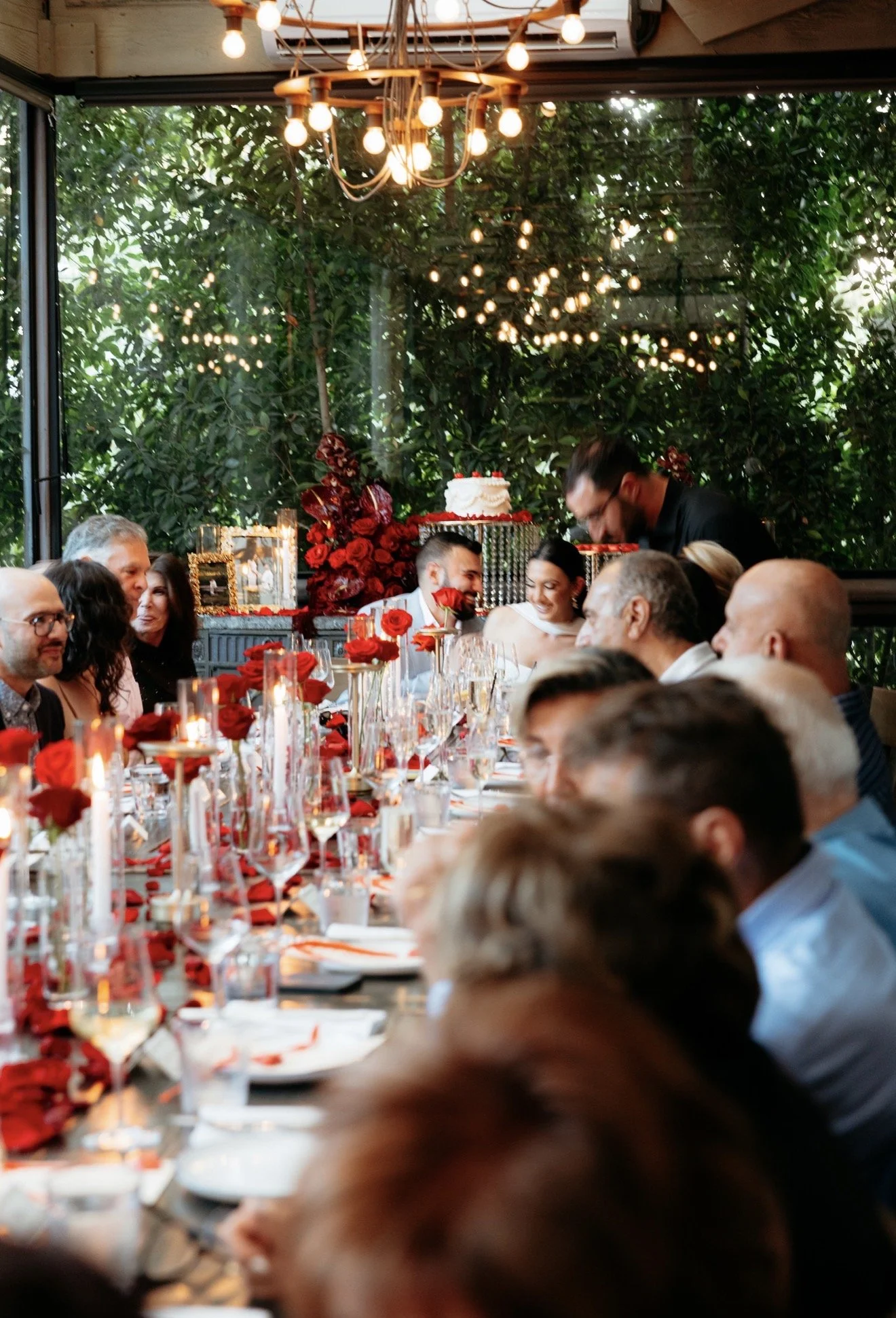 Elegant event setup with white draped backdrop, floral arrangements with red flowers, candles in glass holders, and white tablecloths