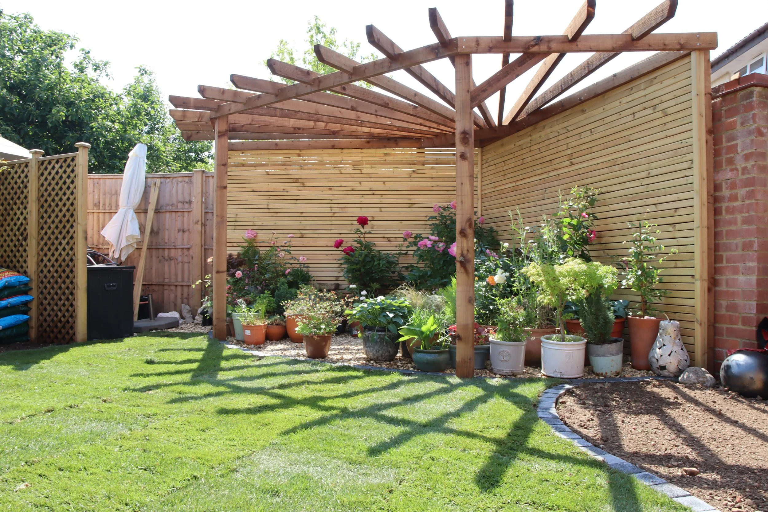 Completed timber pergola with screening, planted pots and lawn