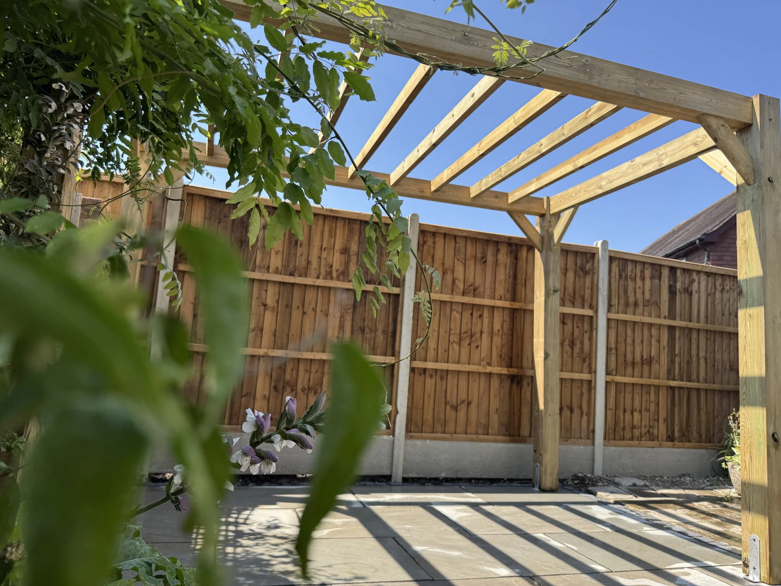 Timber pergola over a paved garden seating area beside fencing