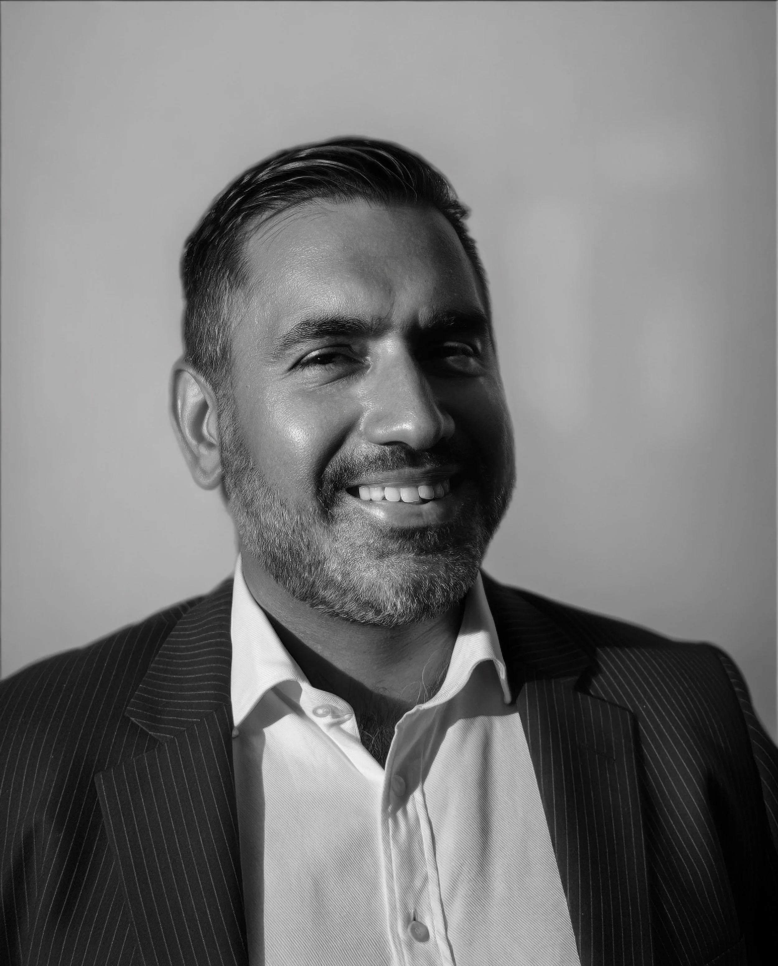 Black and white portrait of a smiling man with short hair, beard, wearing a suit and collared shirt.