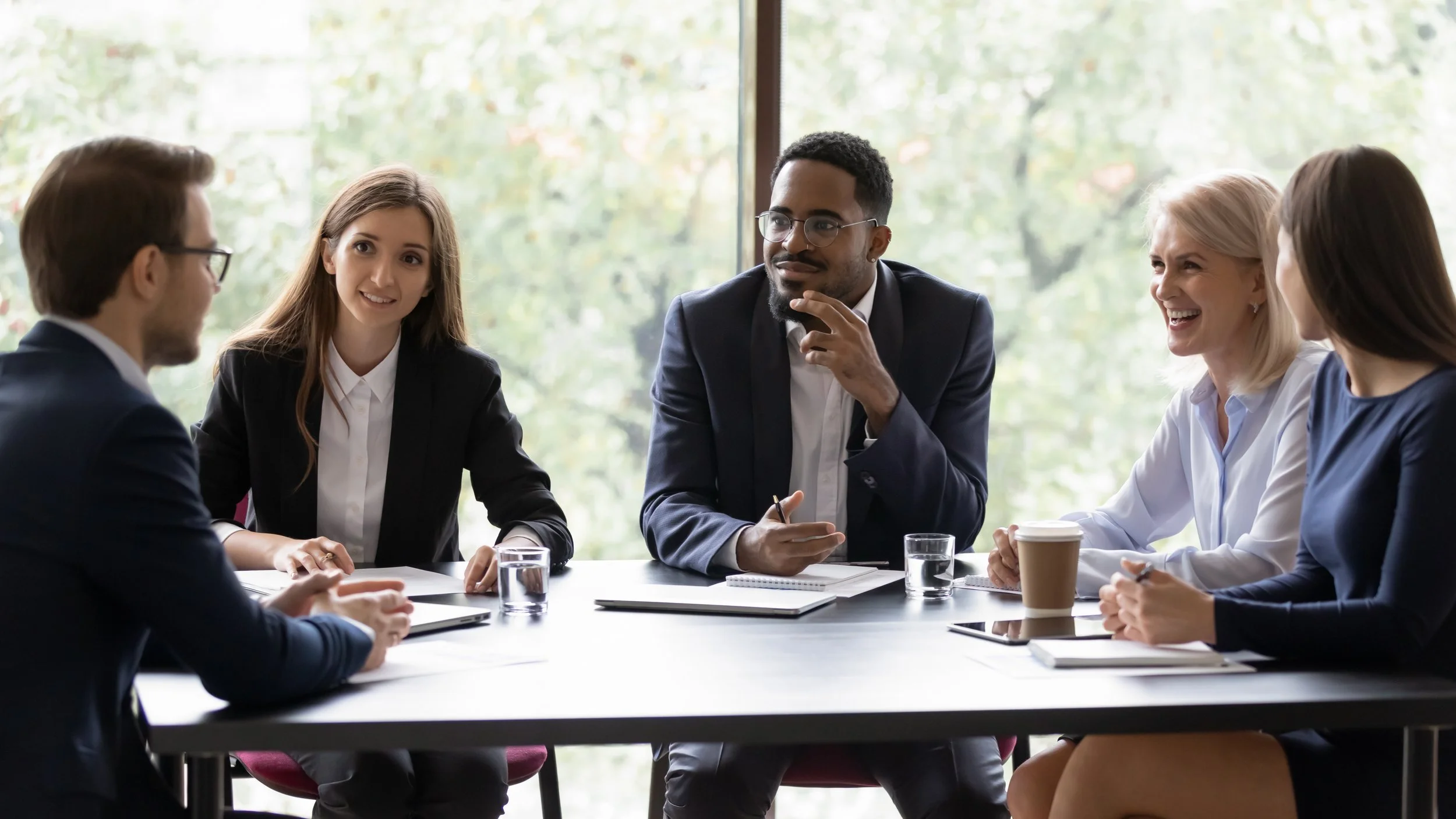 Five diverse professionals engaged in a discussion around a conference table.