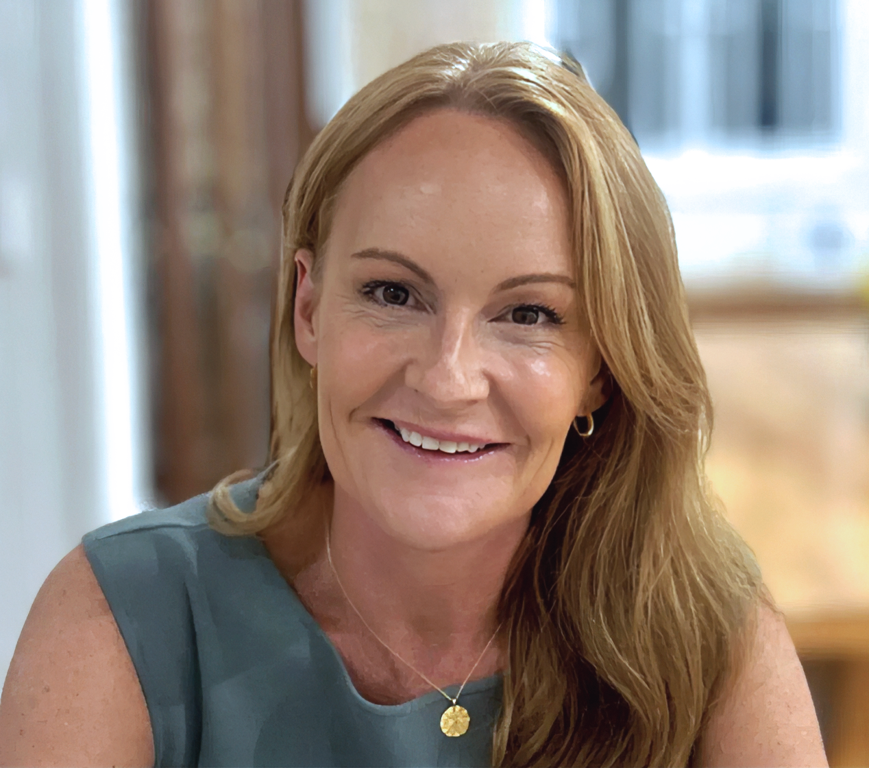 A woman with long red hair smiling in an indoor setting.