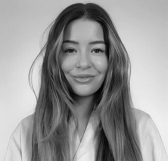 A young woman with long, wavy hair and a subtle smile, wearing a light purple top against a plain, light background.