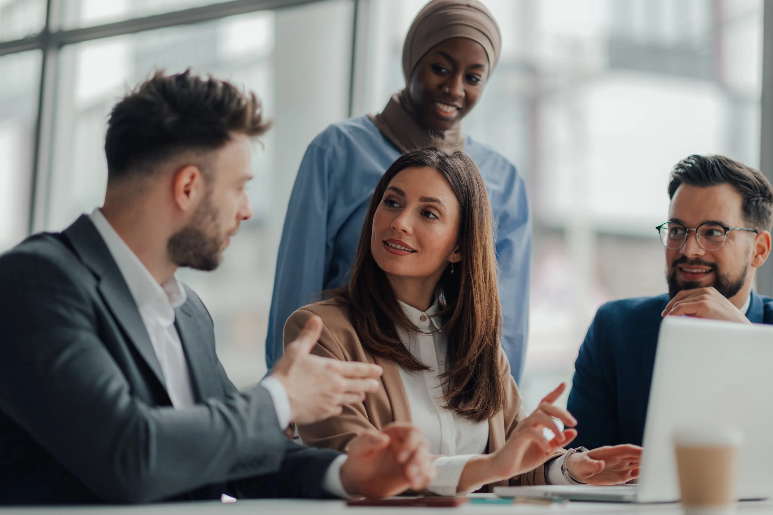 Four diverse professionals having a discussion in a modern office with glass windows.