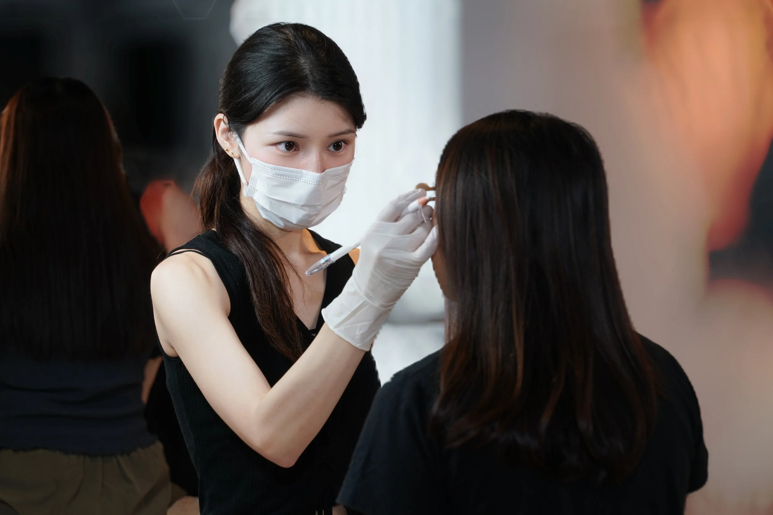 A woman wearing a face mask and gloves is administering a vaccine injection to another woman with dark hair.