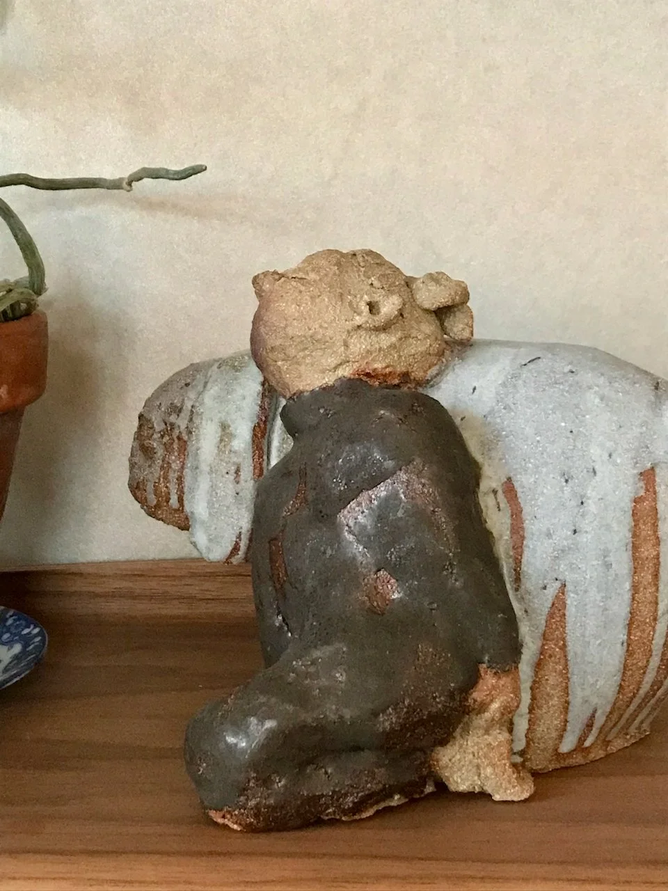 jente og kanin i steingodsleire, jentefigur i brun glasur, kanin i lysgrå glasur, står på hylle med plante ved siden av