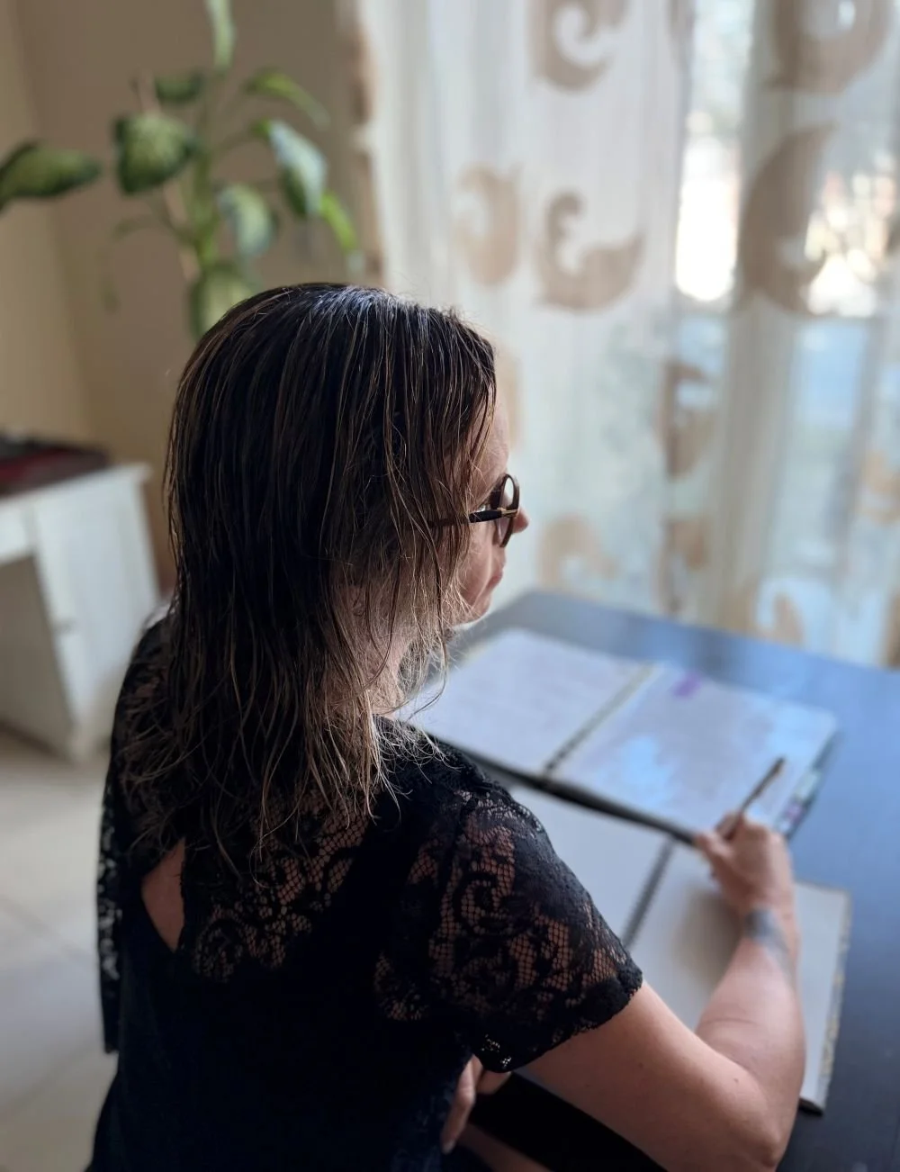 Michela Modolo sitting at a desk writing with glasses on, hand poised with pen, viewed from behind