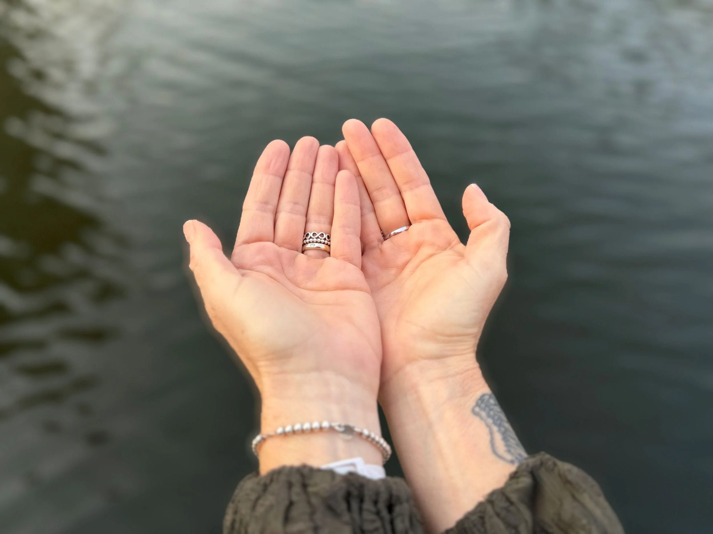 Michela Modolo’s open hands in water showing jewellery and tattoo
