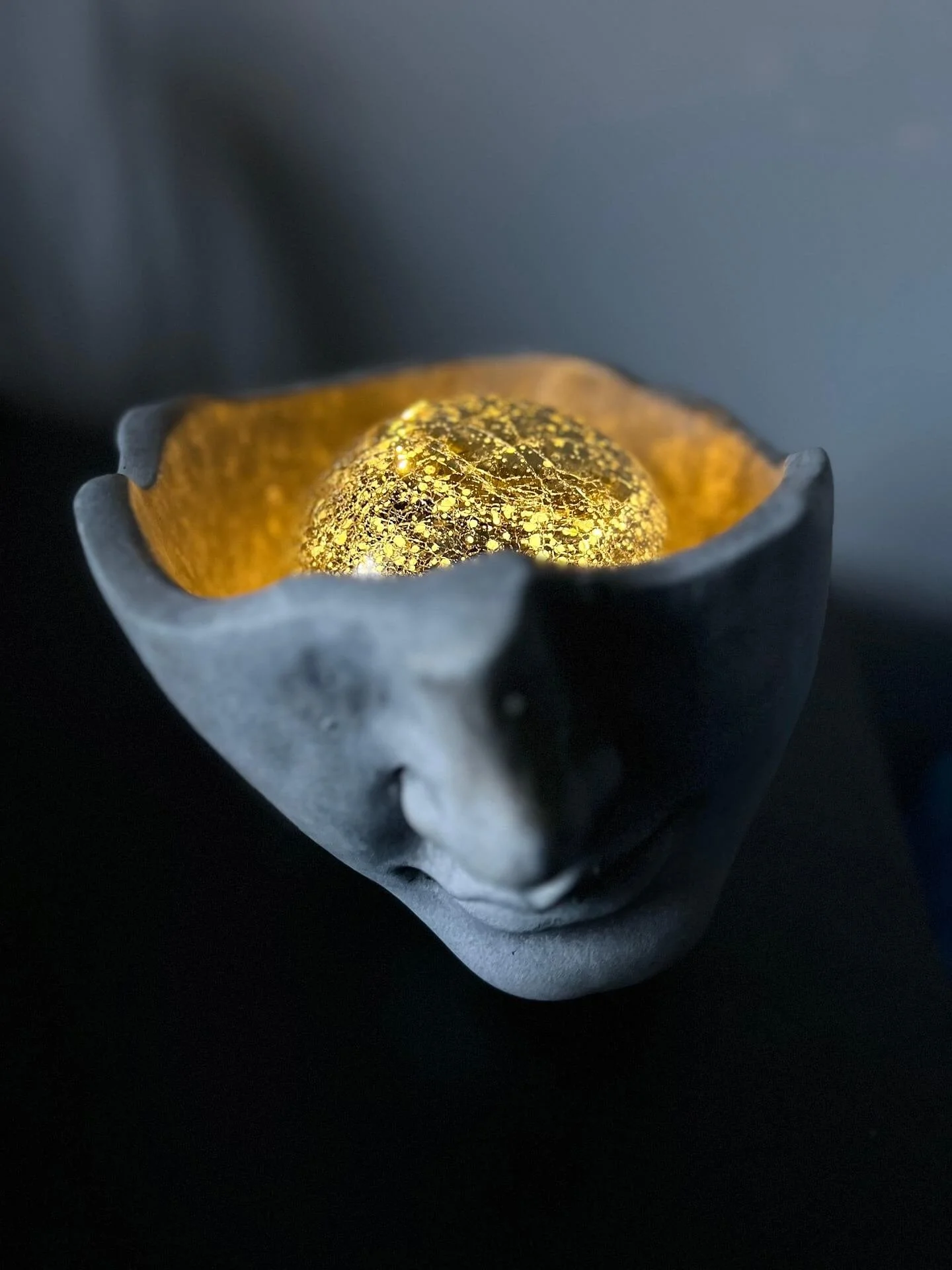 A grey sculpted head cut of below the eyeline to reveal a golden sphere of light where the brain should be