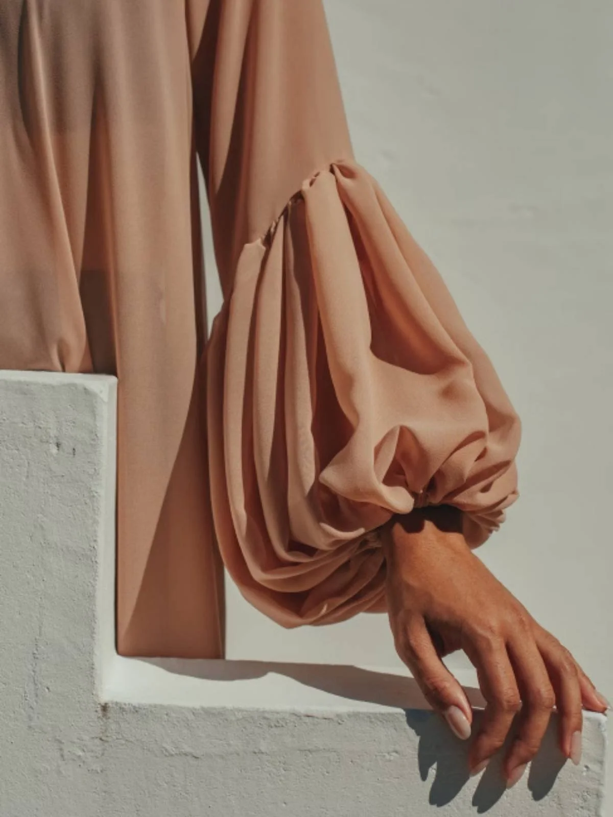 Close-up sleeve detail with hand on white wall.