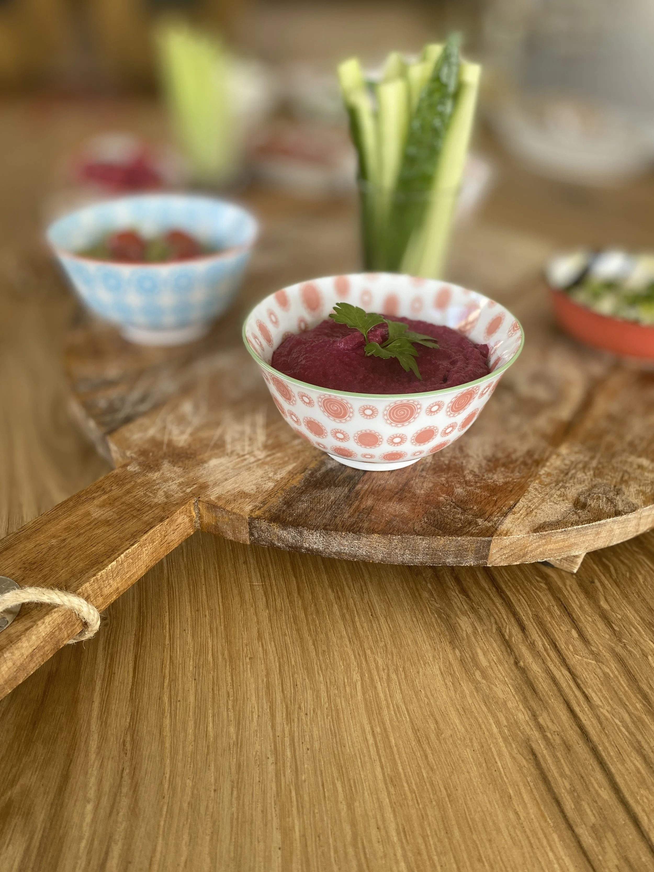 A bowl of beet hummus garnished with a sprig of parsley on a rustic wooden serving board.