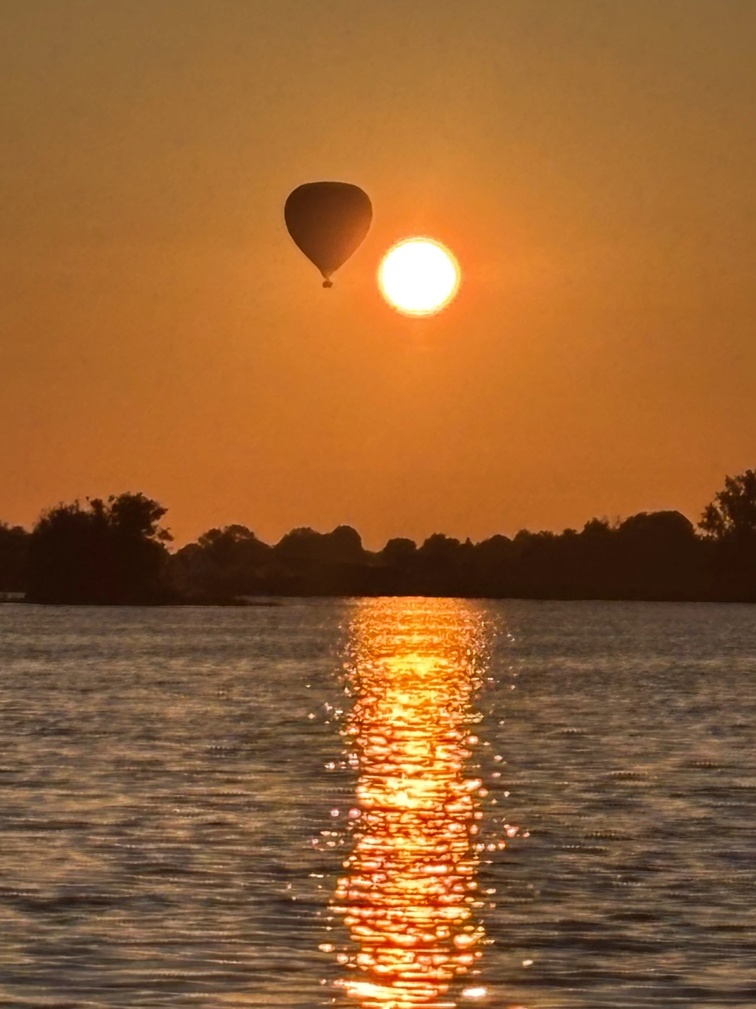 A hot air balloon floating in the sky during a sunset over a body of water with trees in the background.