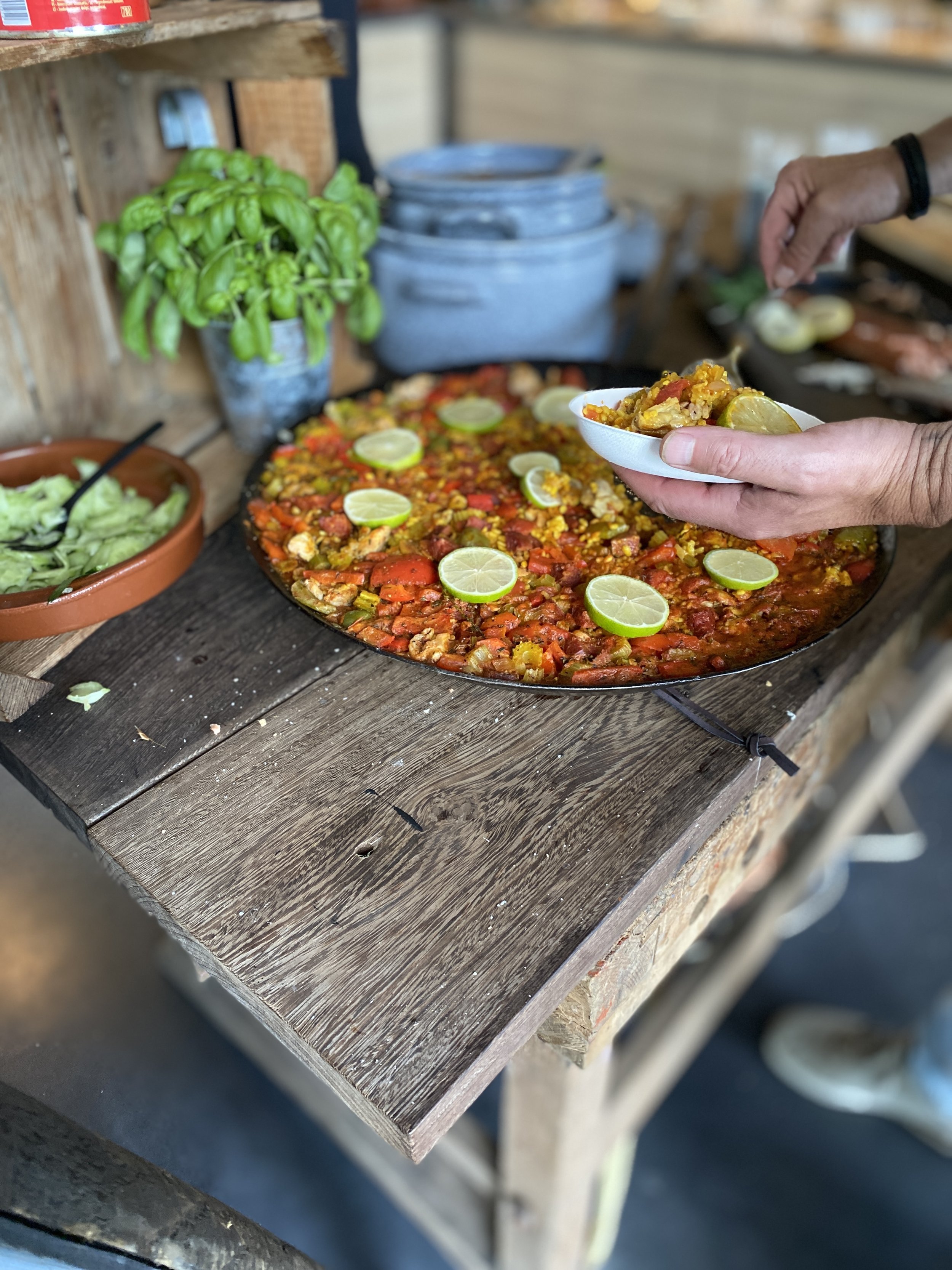 Person serving a slice of vegetable pizza with lime slices on top at an outdoor counter.