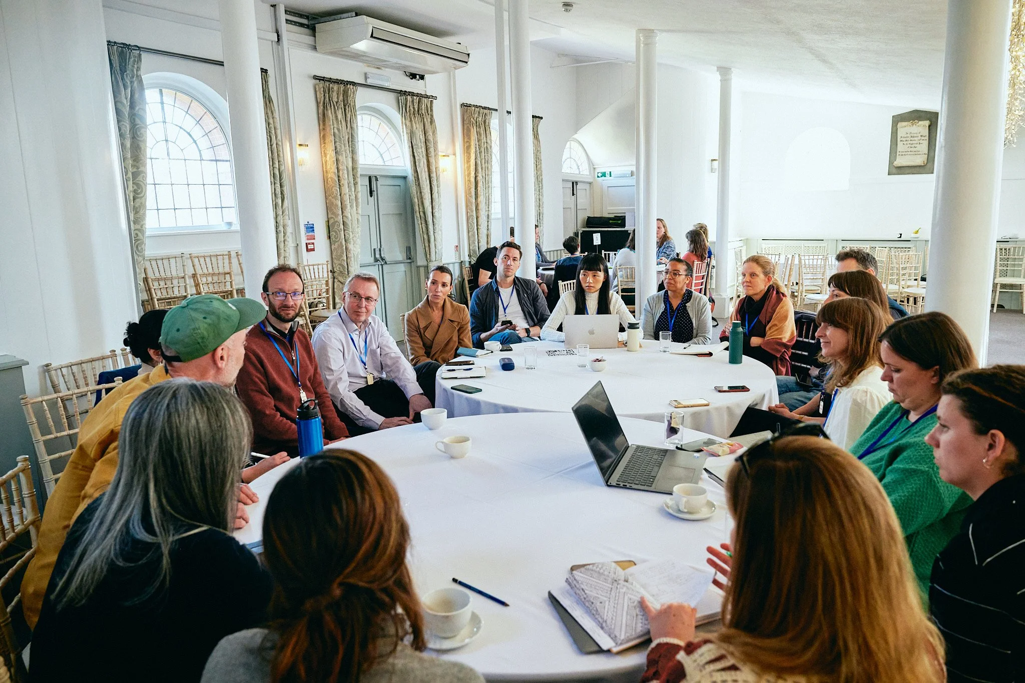 A group of people sitting around two tables that are pushed together. They are a breakout group, in a bright and light room.