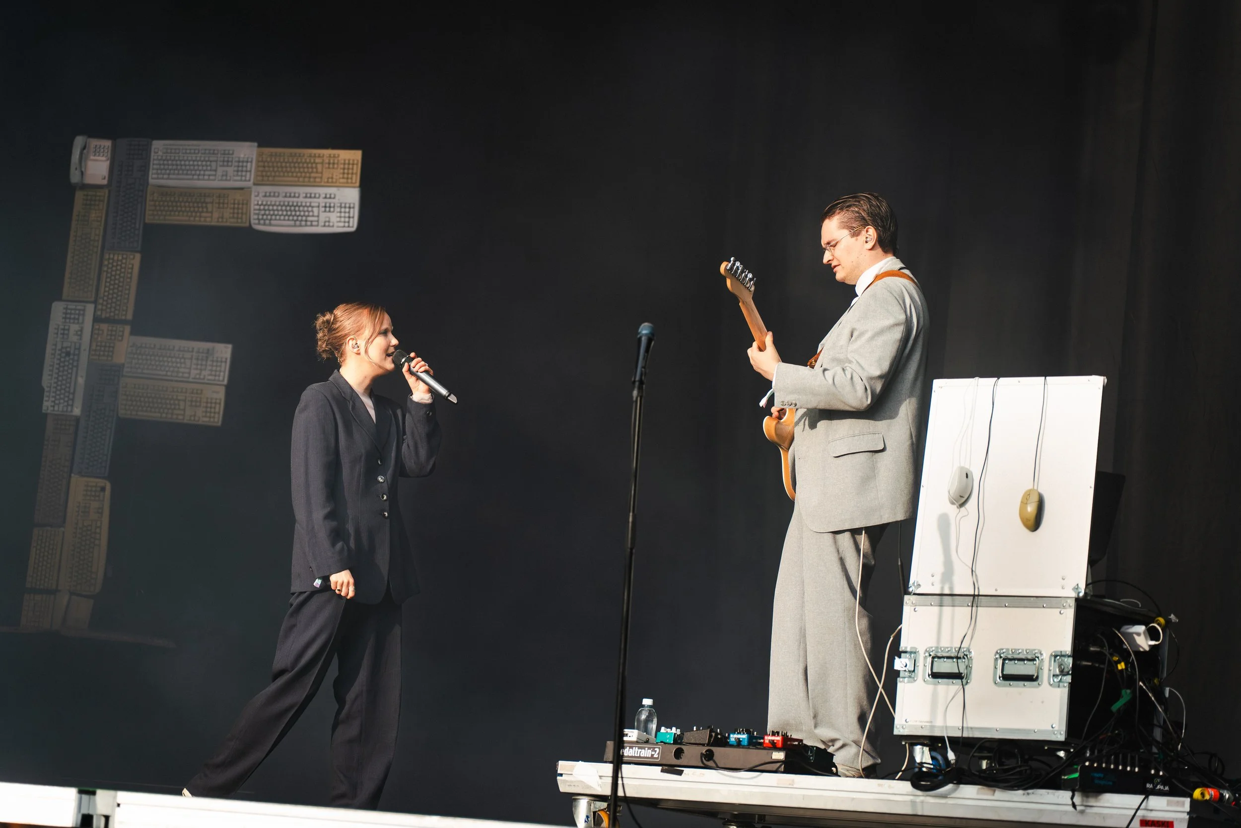 Nainen laulaa mikrofonilla ja mies soittaa kitaraa lavalla.