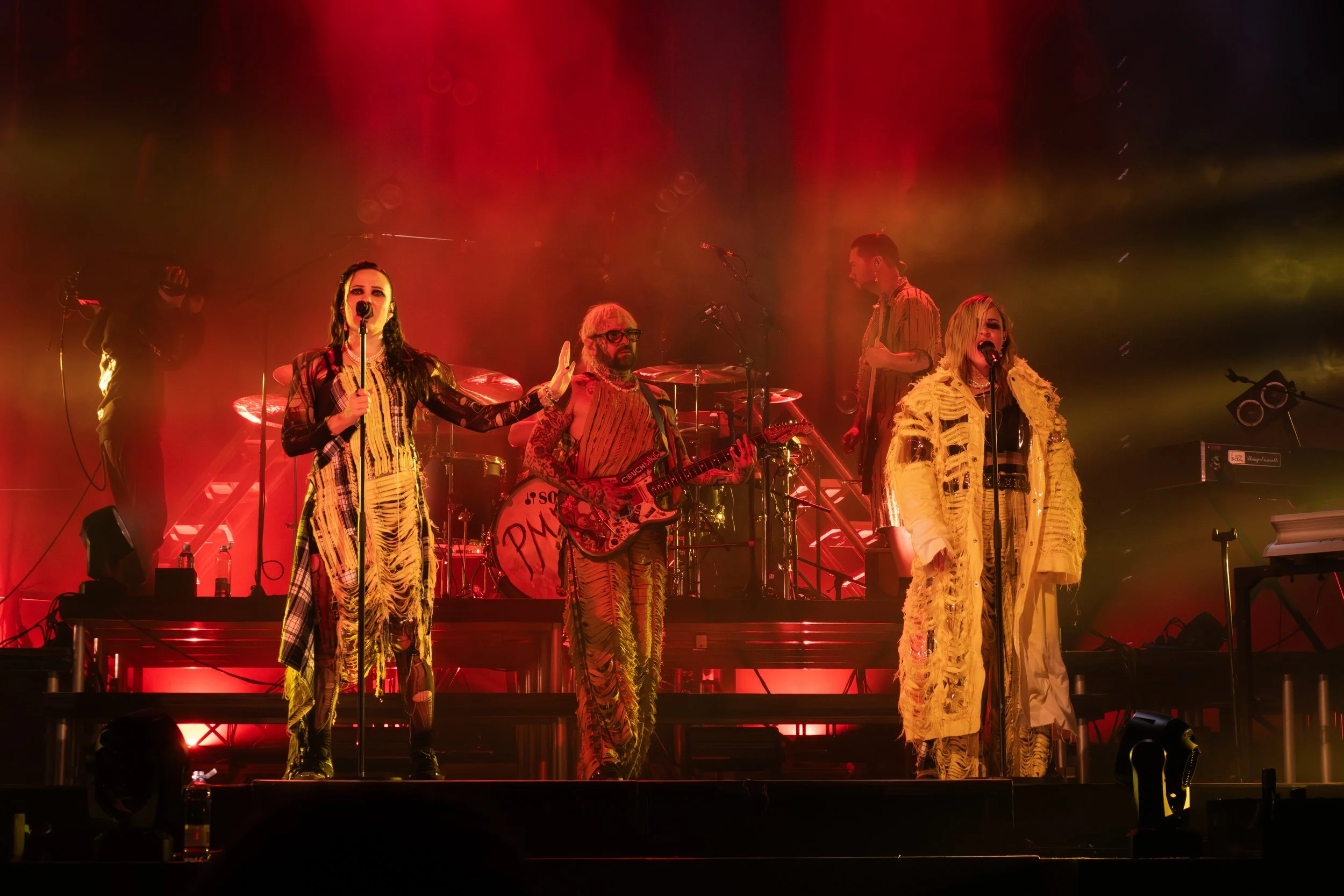 Nelikielinen musiikkiesitys lavalla, jossa kolme naista ja kaksi miestä, valaistus punainen ja vihreä, musiikkivälineitä ja mikrofoneja.