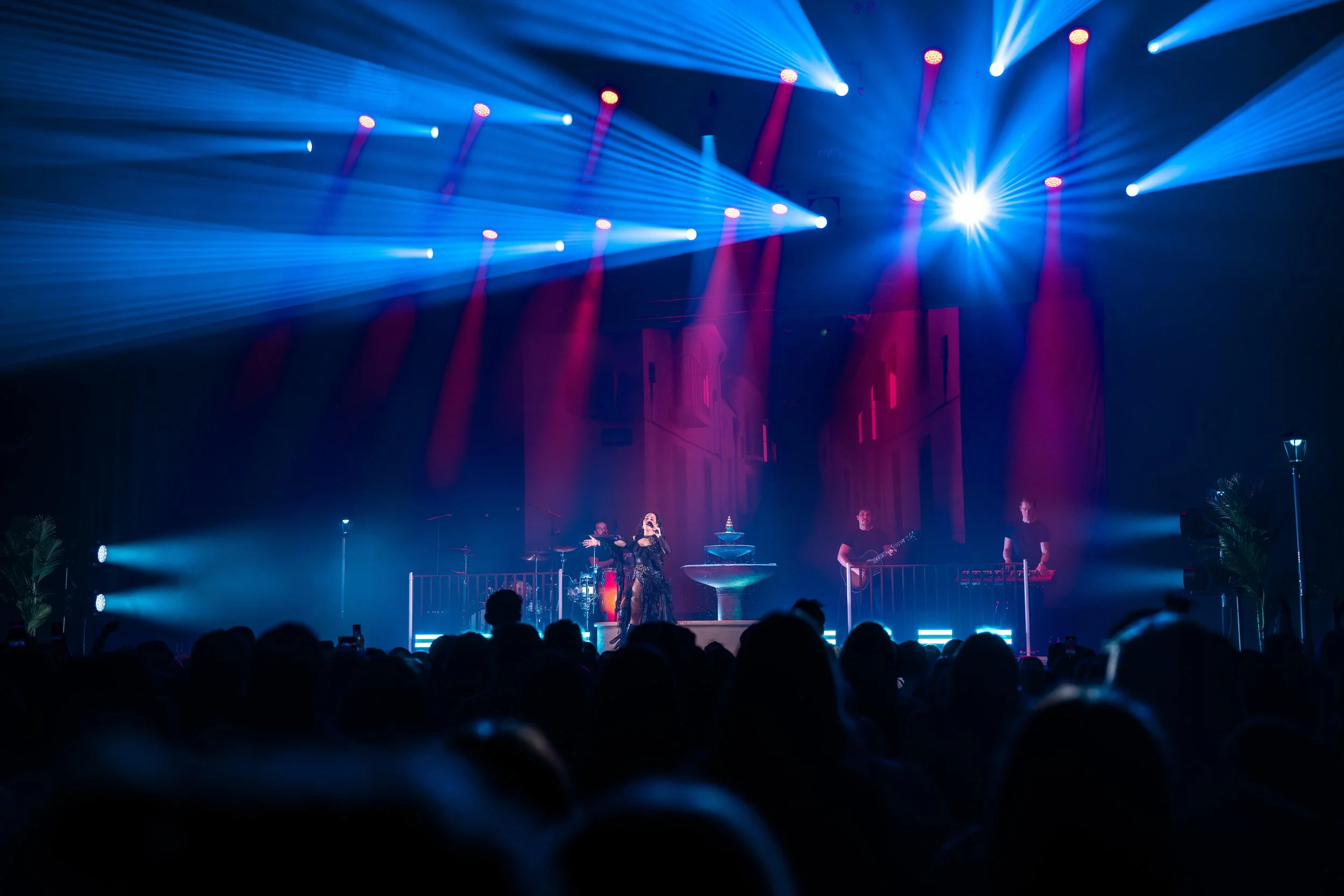 Yleisön edessä esiintyvä muusikko ja bändi lavalla valojen loisteessa, taustalla rakennusten siluetti.