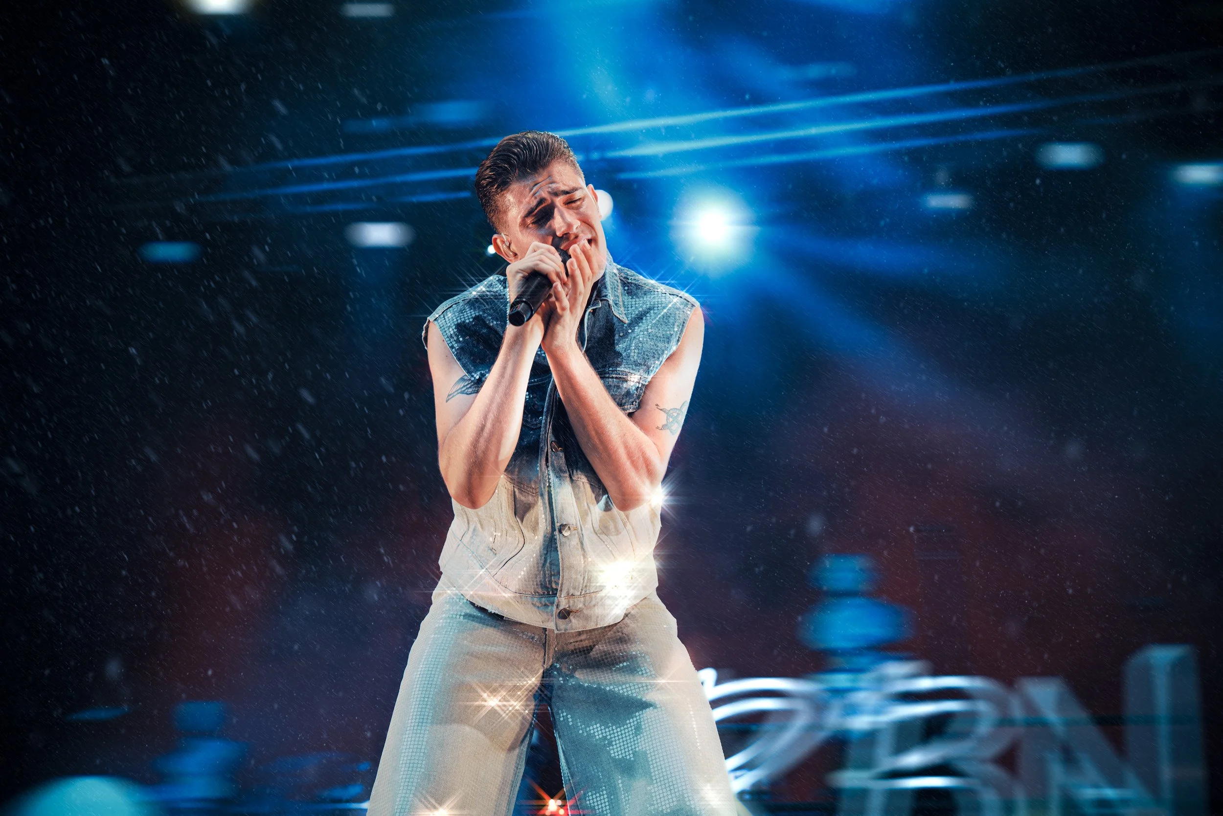 Sooloja laulava mies esiintymislavalla, taustavalot ja lavavaloja ympärillä.