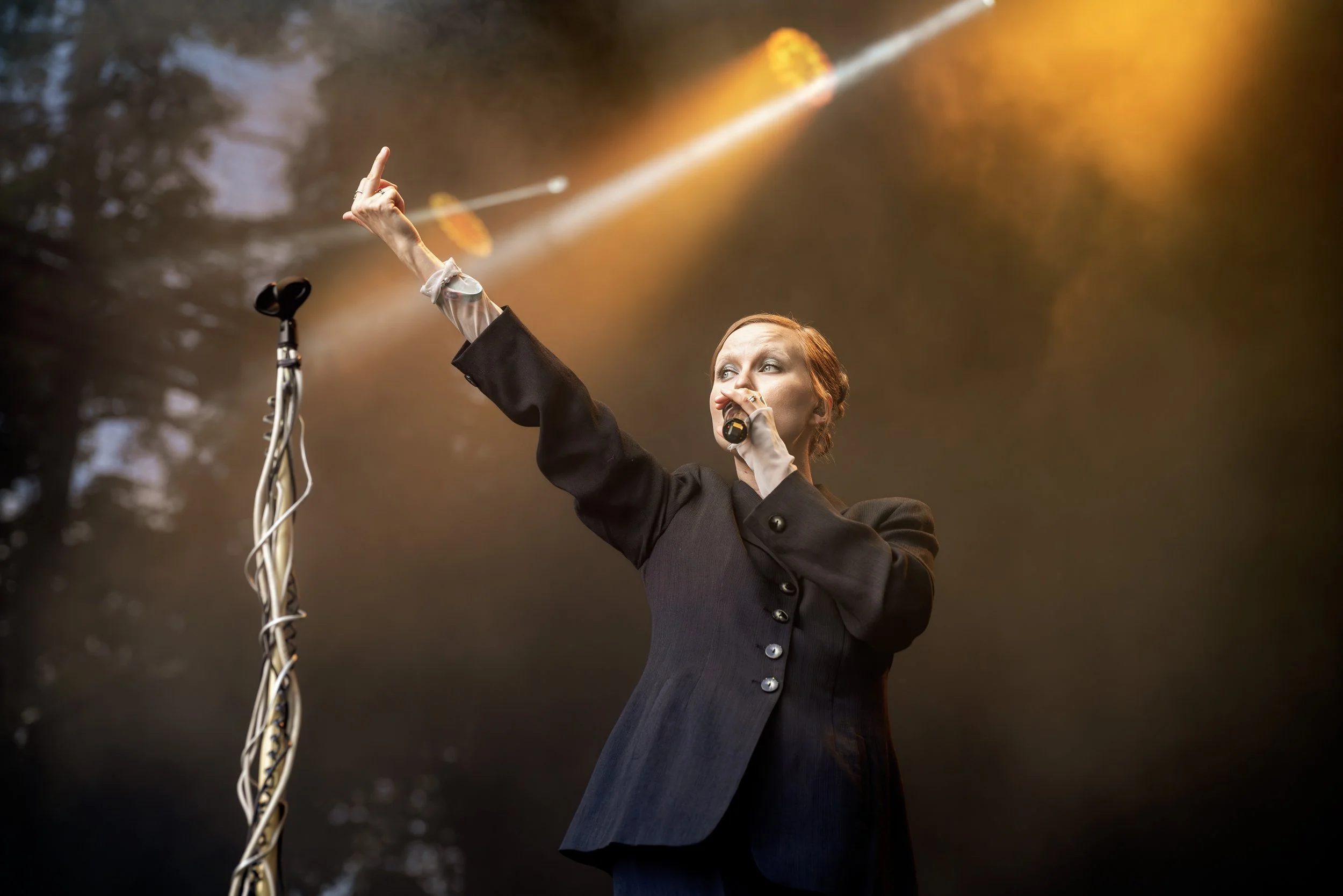 Naista esiintymässä lavalla, käsissään mikrofoni ja tekevä liikkeitä musiikin tahdissa, taustalla värikäs valaistus.