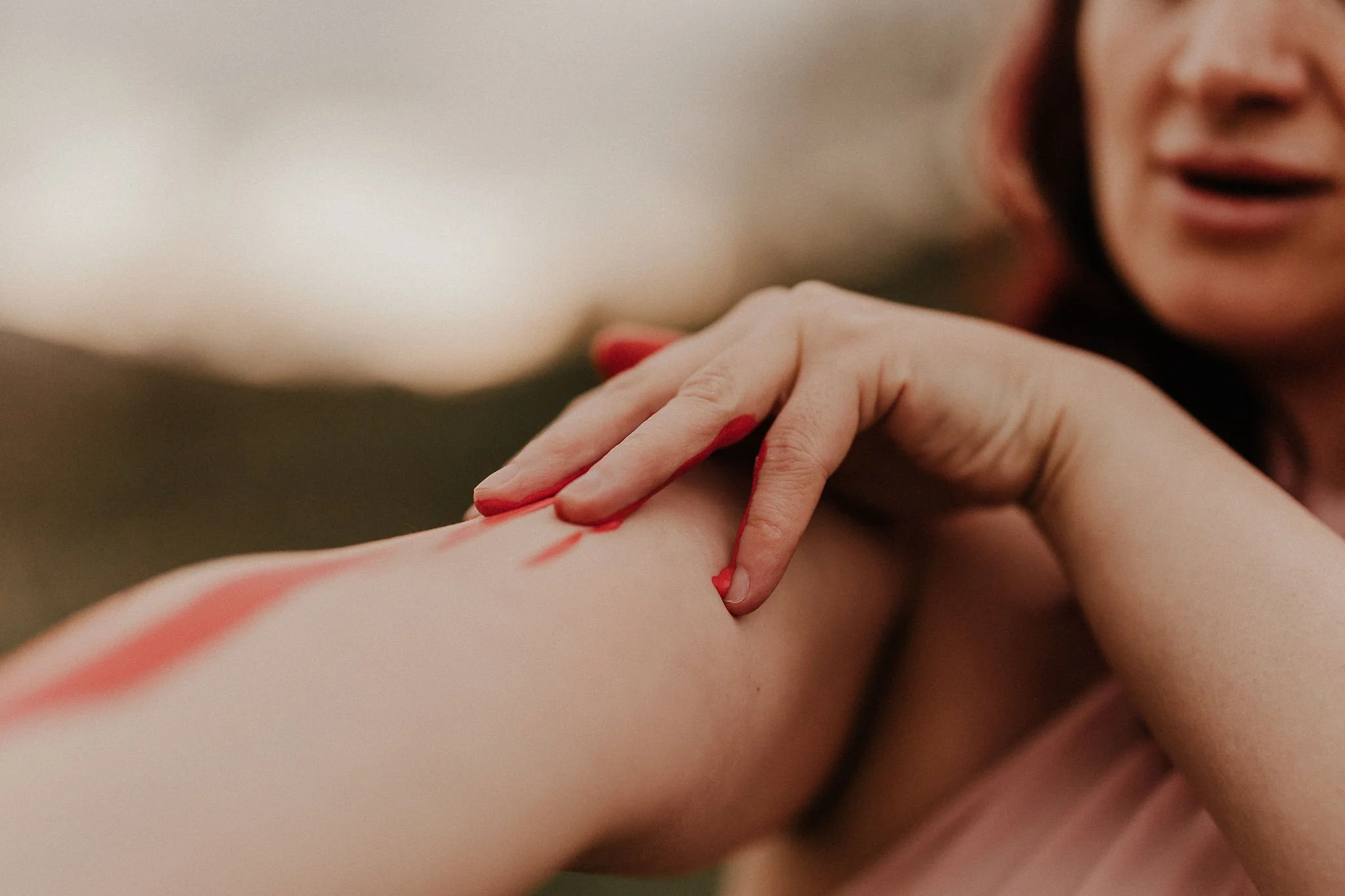 Person applying red paint to their arm outdoors.