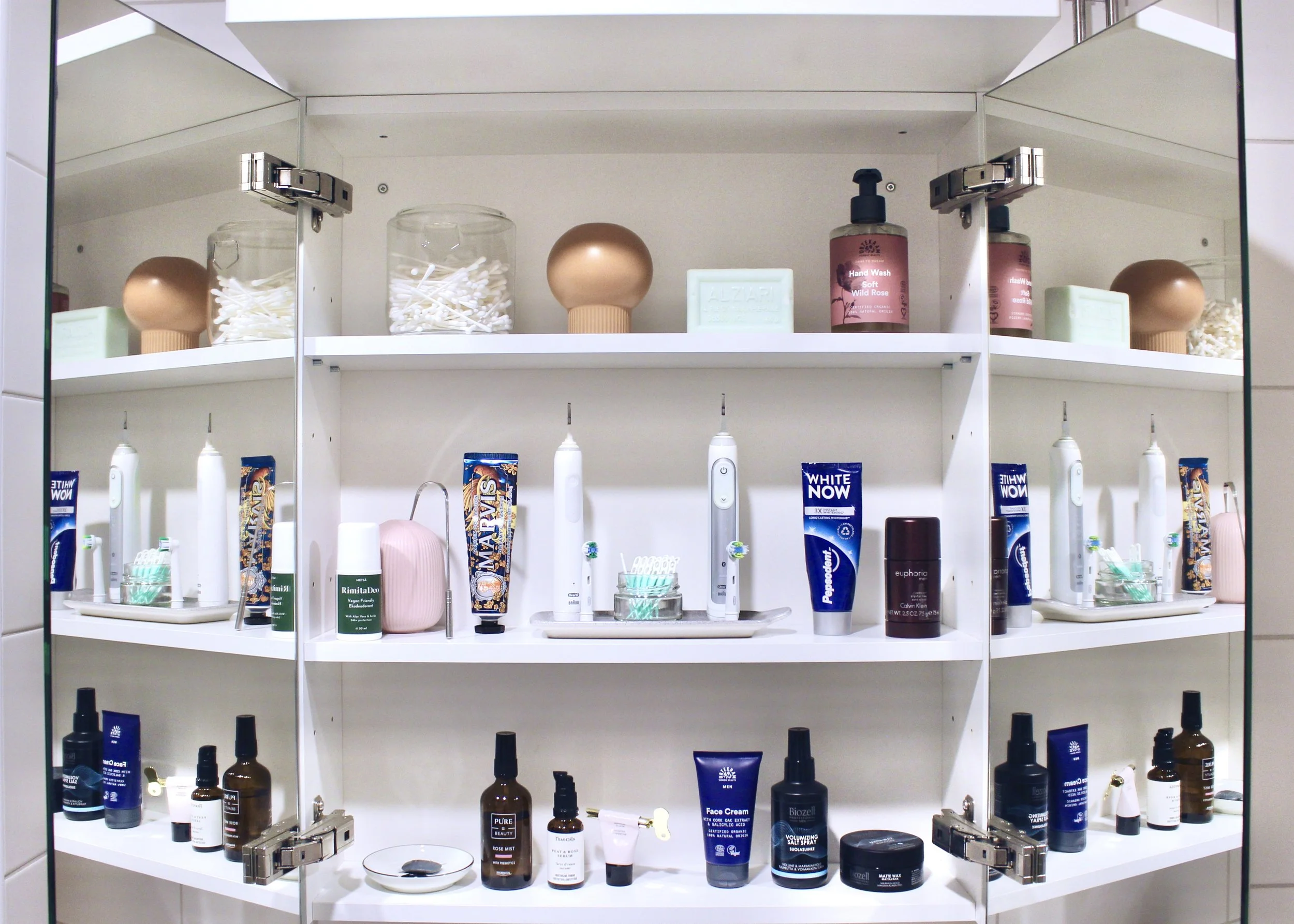 Kuva avonaisesta peilikaapista, jossa hyllyillä tuotteita järjestyksessä