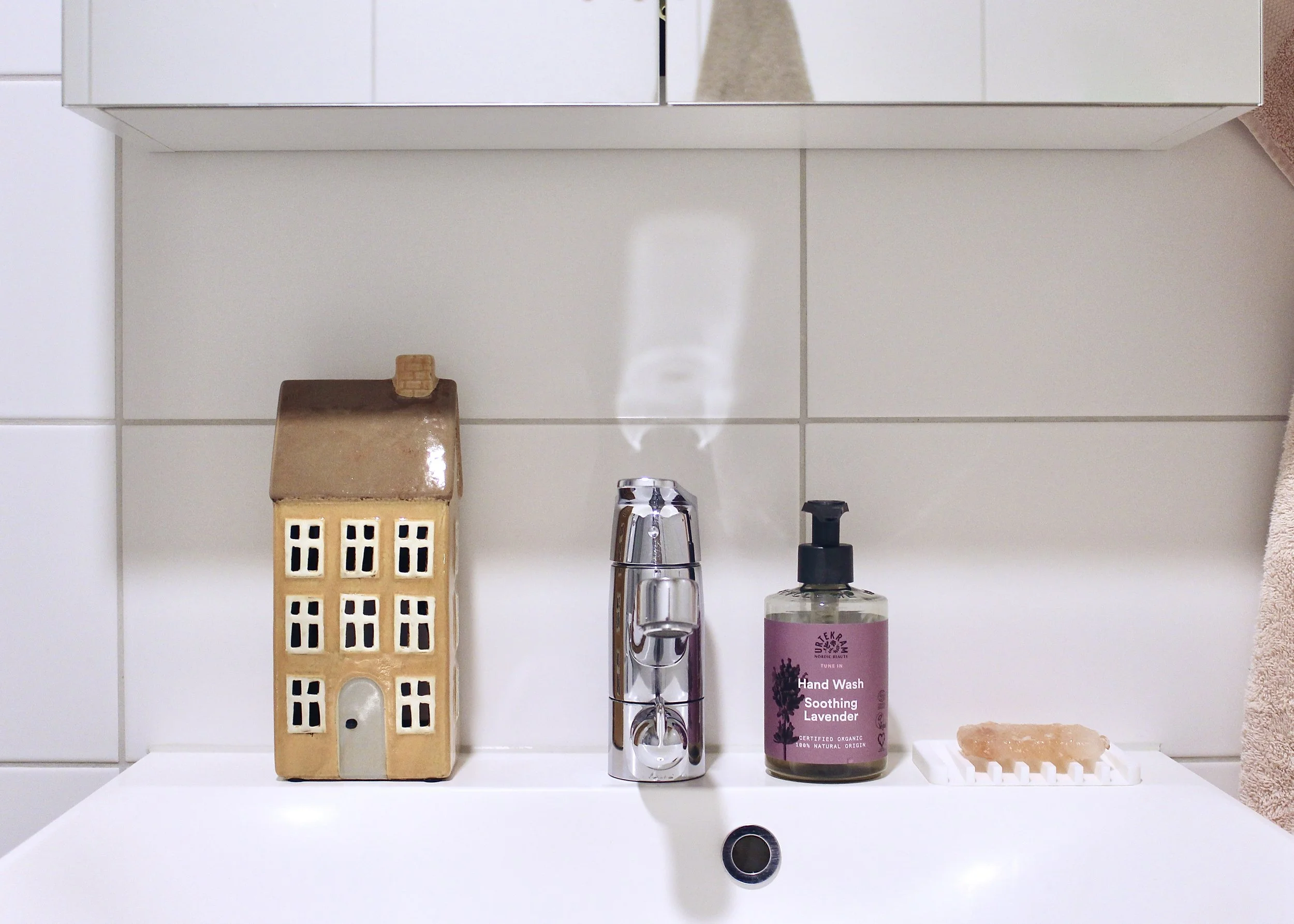 Kuva edestä lavuaarista, jonka reunalla keraaminen talo ja saippuapullo