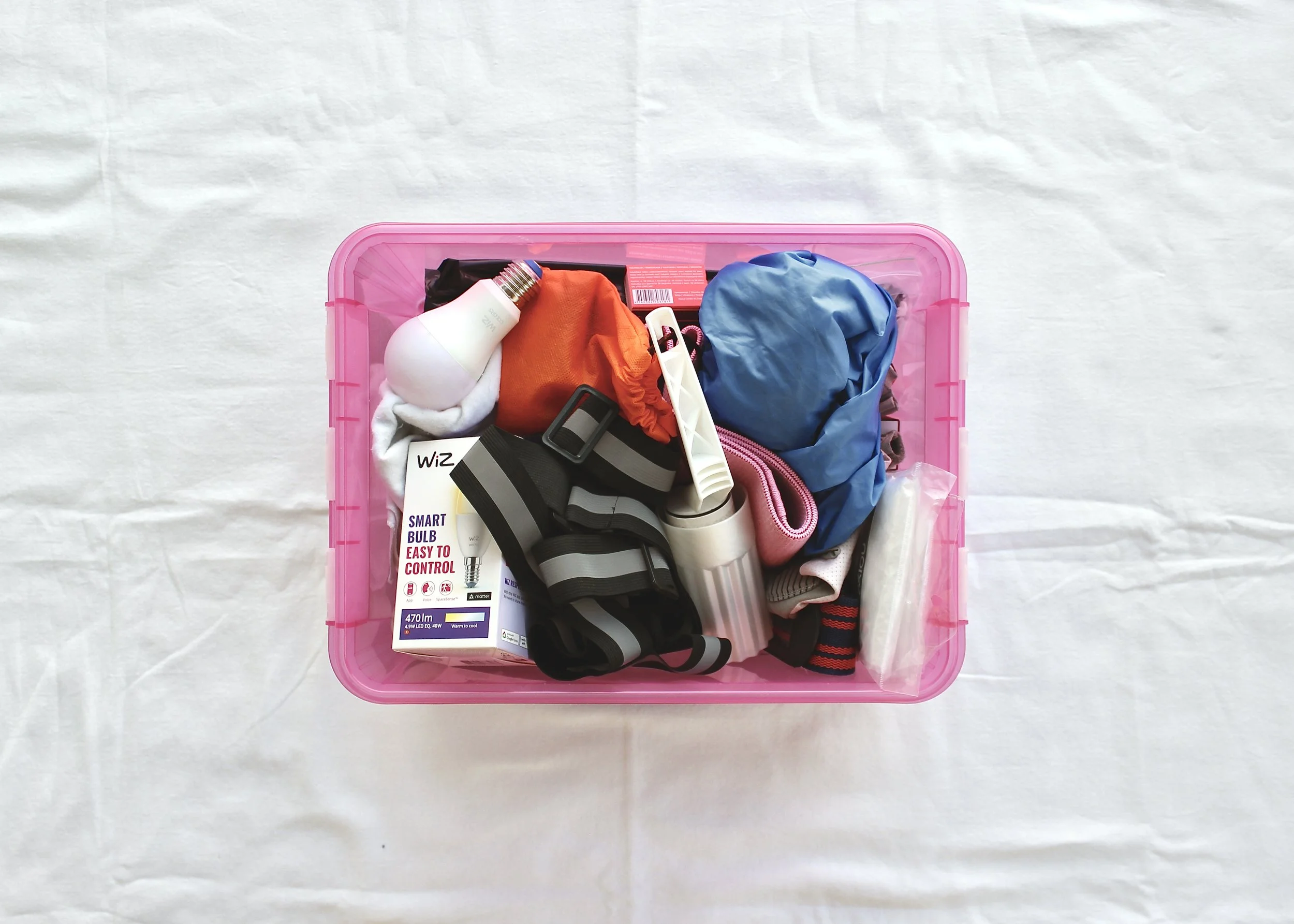 Kuvan keskellä muovilaatikko, jonka sisällä on tavaraa sekaisin