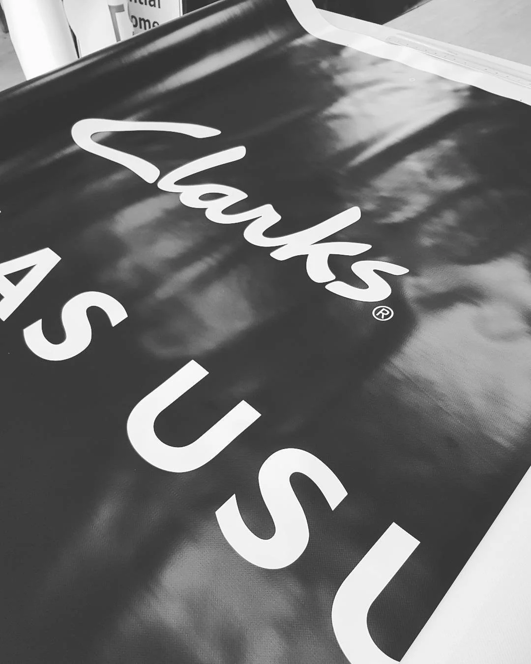 Close-up of a large sign or banner with shiny black surface, displaying the text 'Thanks US' in bold white letters, partially visible.