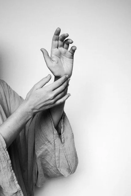 Two hands, one with fingers curled, grasping the wrist of the other hand, against a plain background.