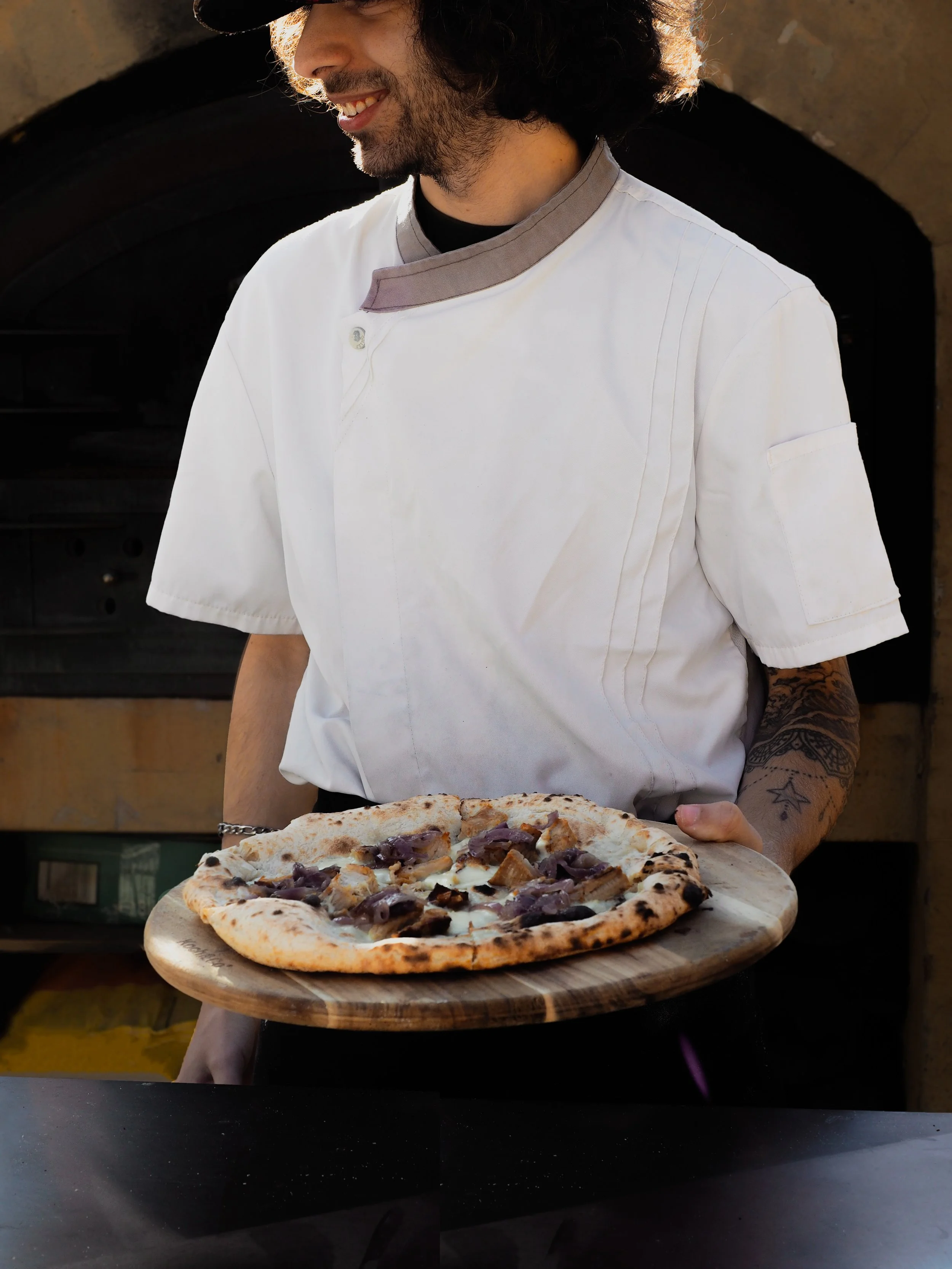 italian pizza chef pizzaioloi sydney in white chef coat holding wood fired pizza