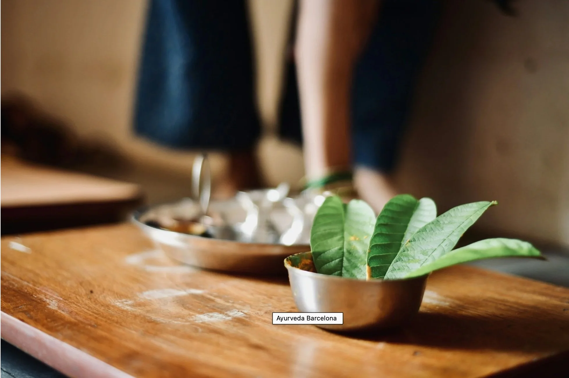 Hojas frescas y utensilios ayurvédicos en bandeja de plata sobre mesa de madera, preparación de una sesión en Ayurveda Barcelona
