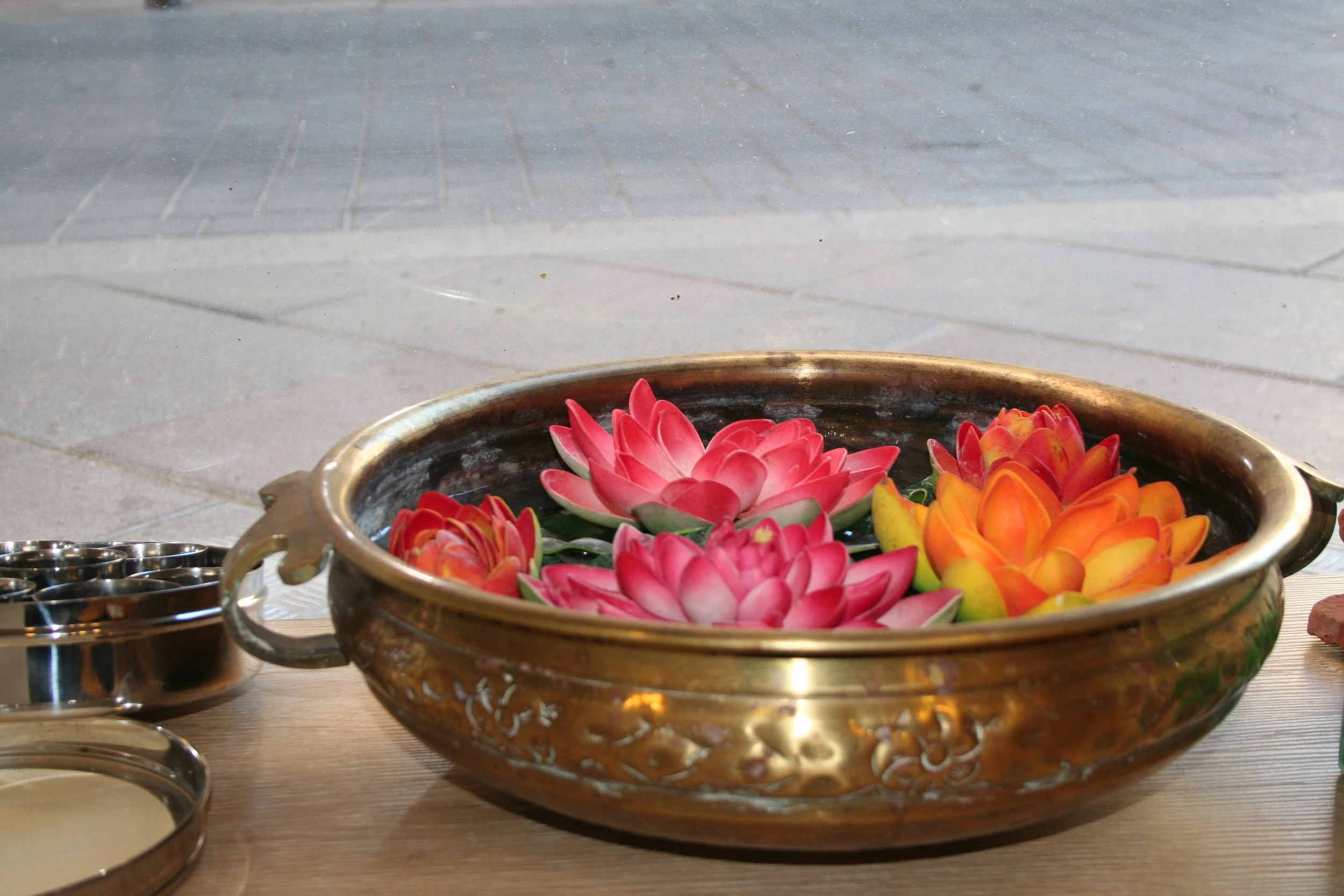 Flores de loto en un recipiente de metal decorativo, con algunos pequeños recipientes de metal a un lado en el Centro Ayurveda Barcelona