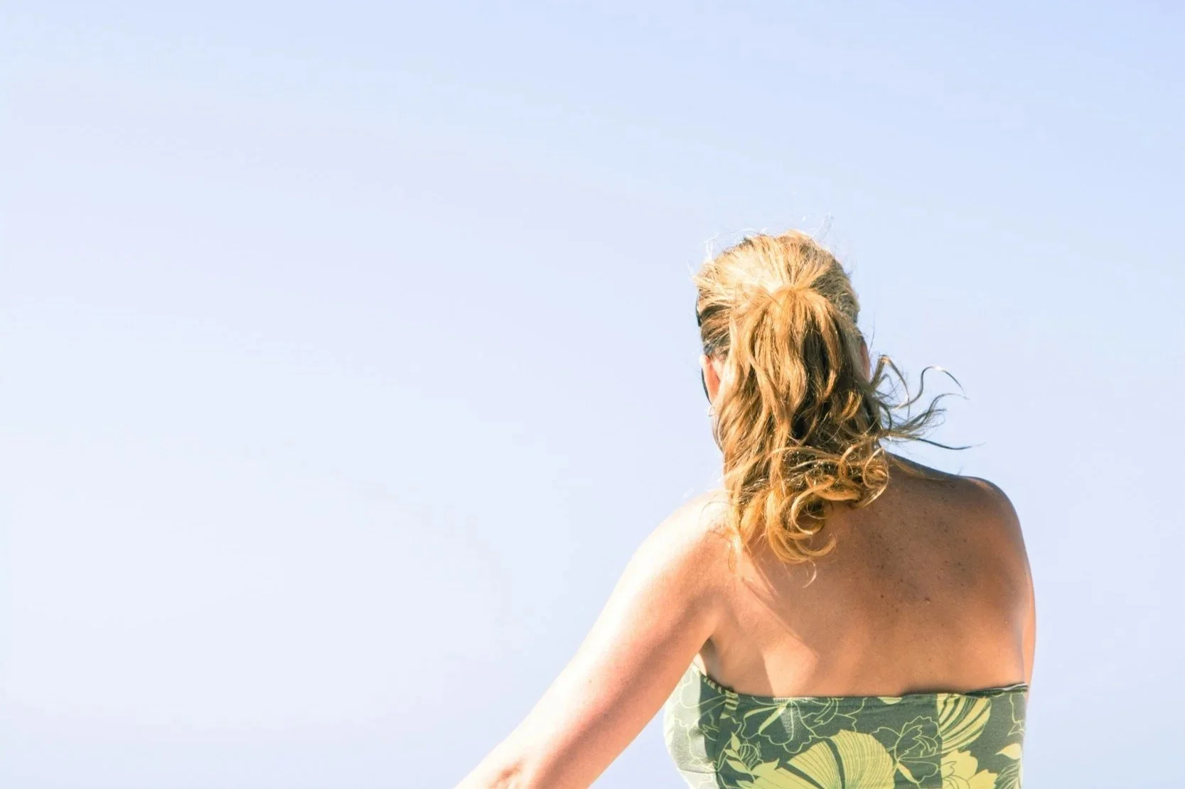 Mujer de espaldas en la playa con el cabello suelto al viento, ilustrando el cuidado capilar ayurvédico en verano