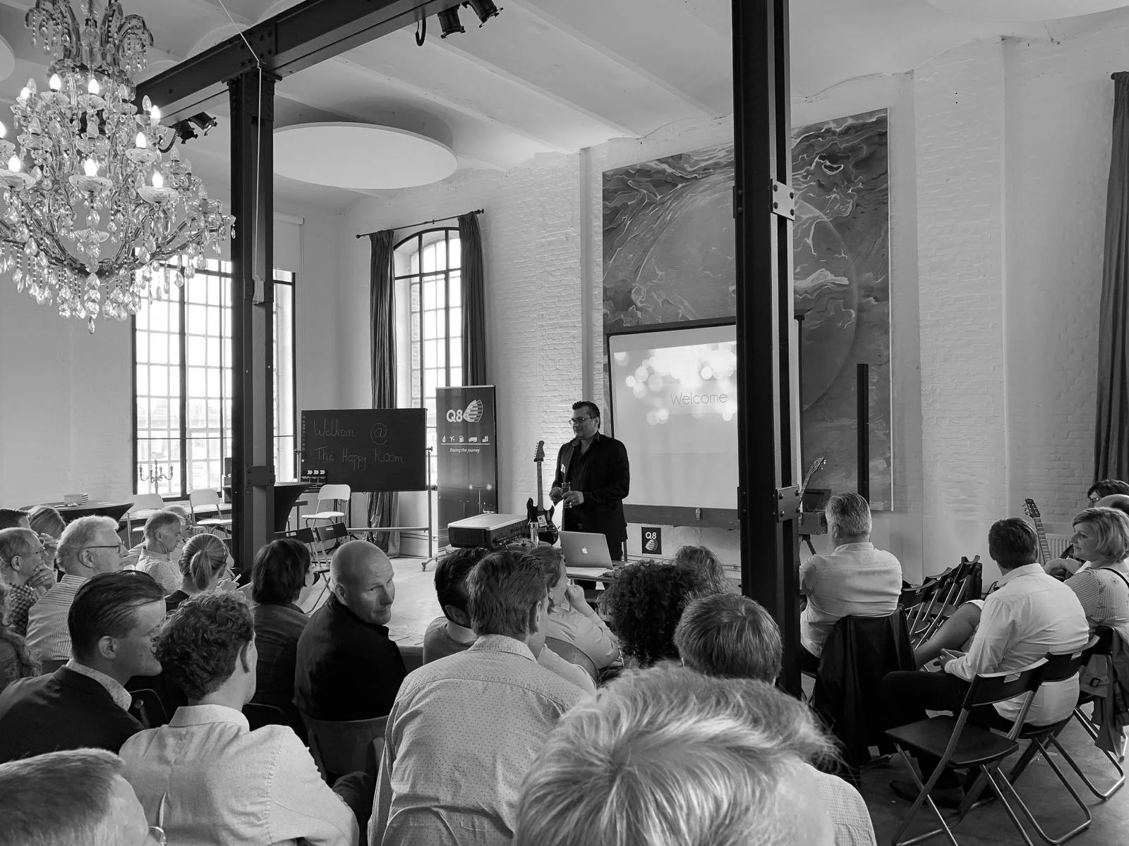 Black and white photo of a man giving a presentation to a seated audience in a room.