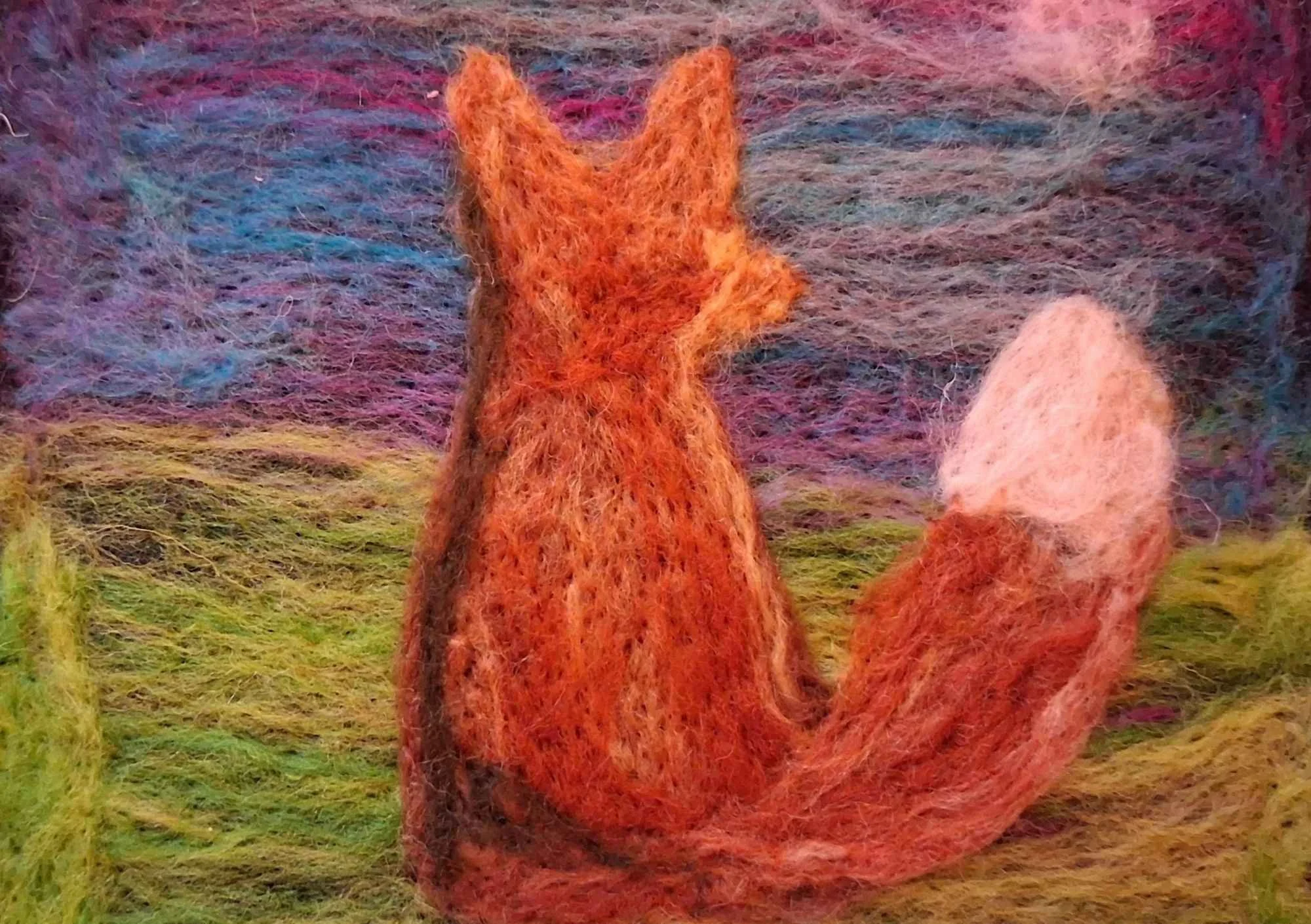 felting artwork showing the back of a fox sitting down on grass