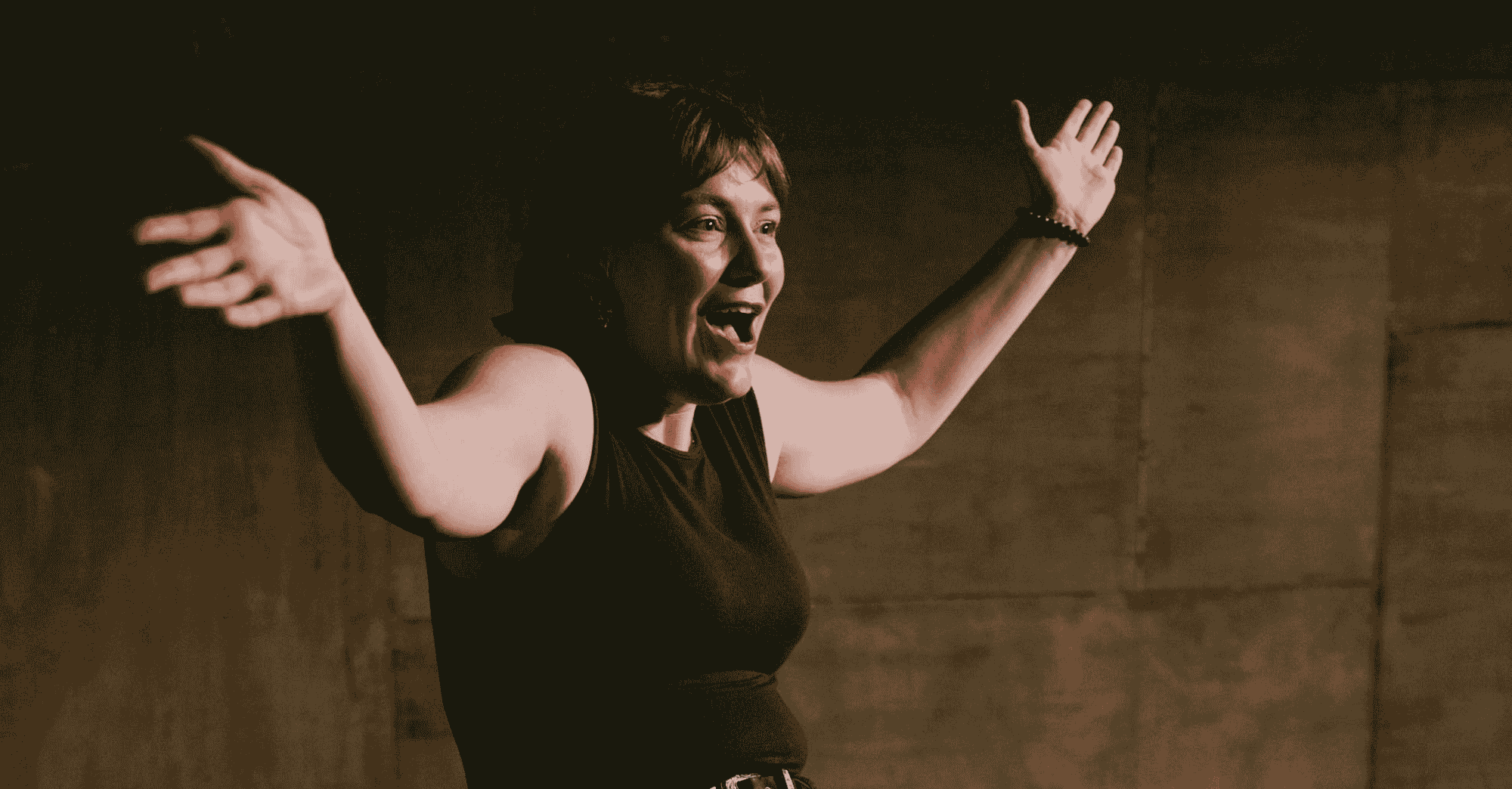 Corinne Harragin is sitting on a stool and has her arms out with a smile on her face