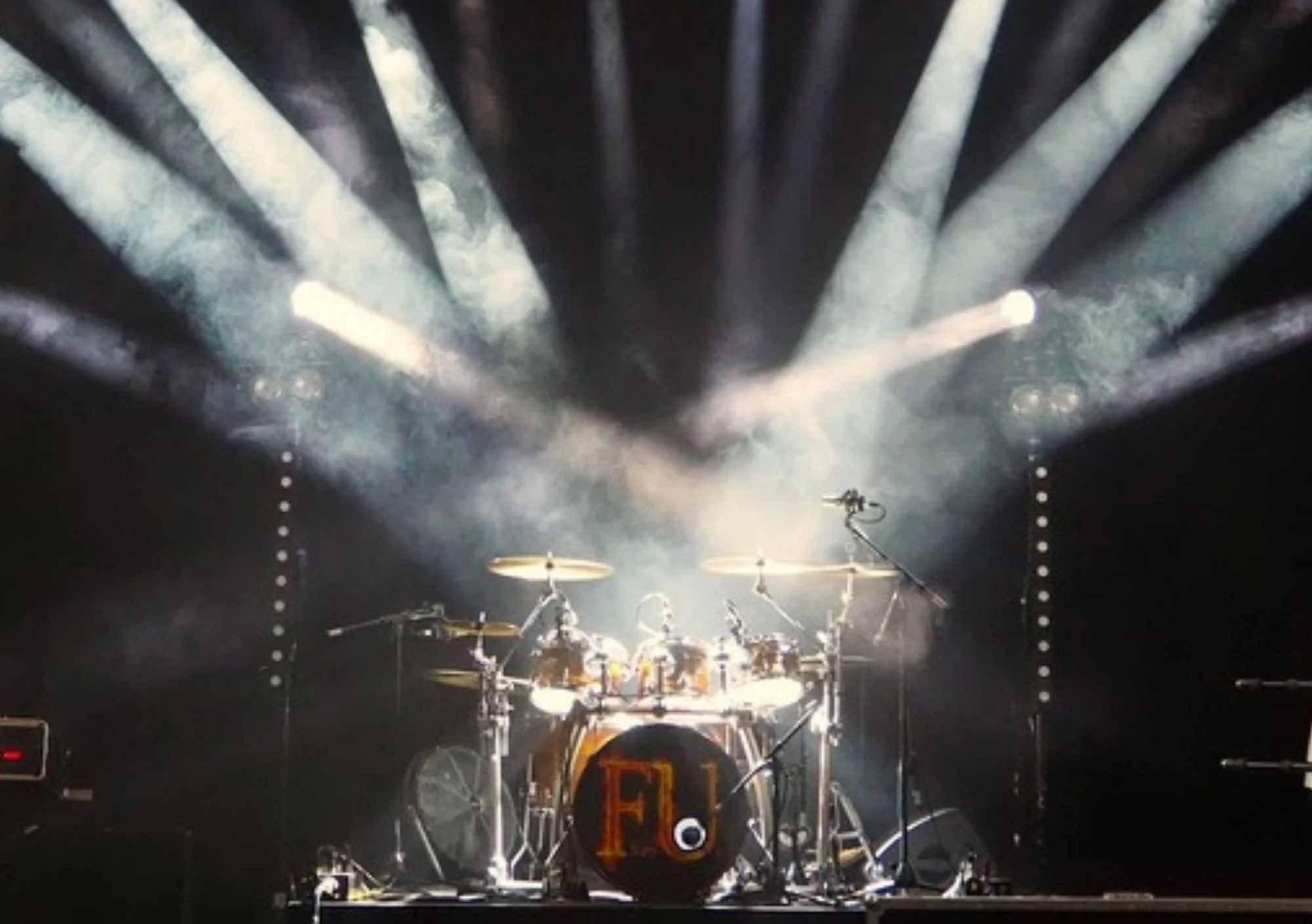 image shows drums in a middle of a stage with spotlights pointing to it