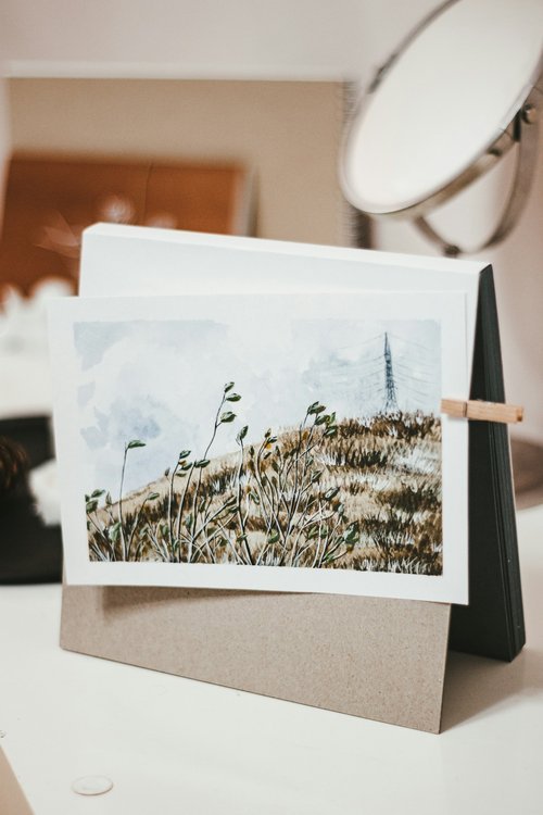 A photograph of a landscape painting of grassy hills with a blue sky and an electricity pylon, set on a stand with a mirror in the background.