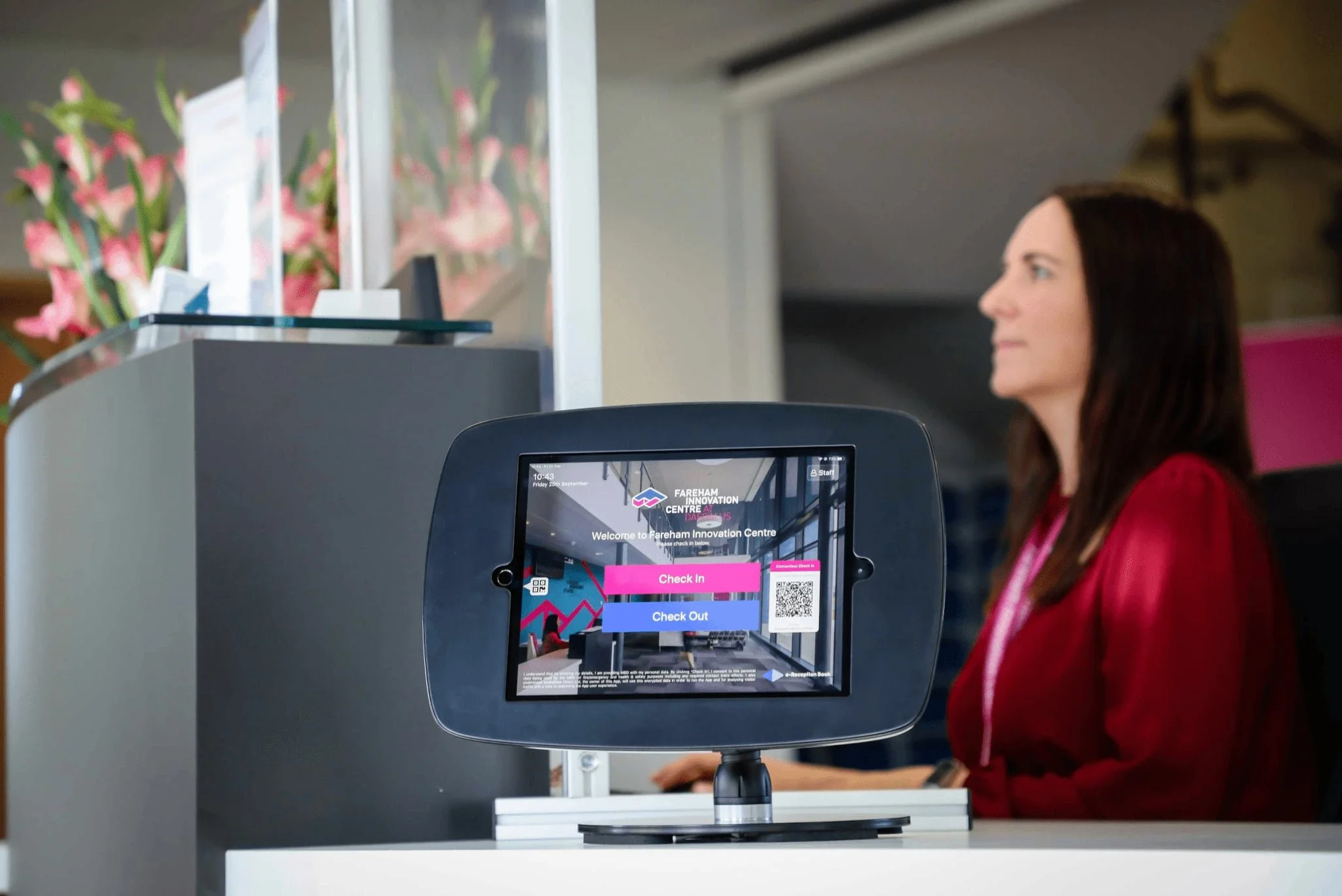 Custr workplace visitor management system in use at Fareham Innovation Centre. The iPad is sat on the front desk with a women working at her computer in the background