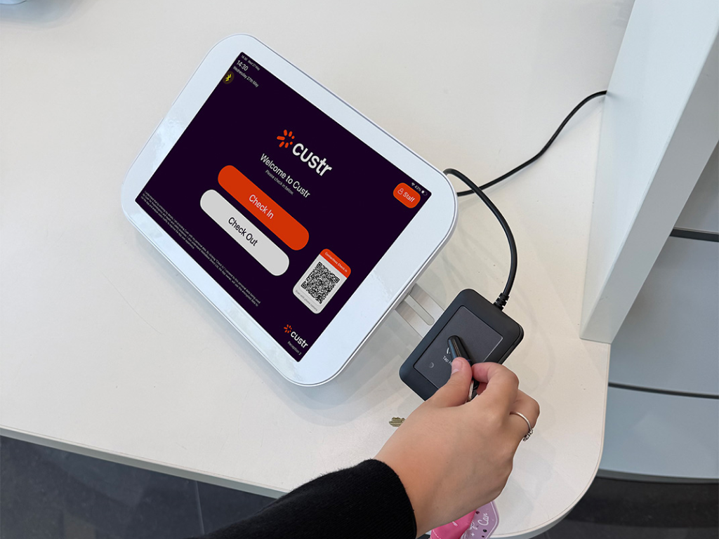 A Custr branded iPad in a white stand, a woman is holding her fob over the RFID reader