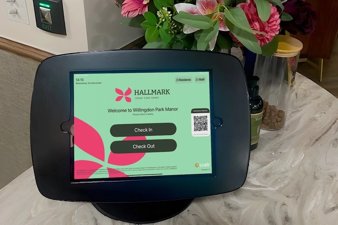 An iPad used to sign in is stationed on the front desk. Behind the iPad is a bunch of pink flowers in a vase.