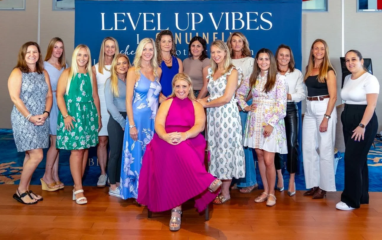 Group of women posing together indoors with a blue sign that reads "Level Up Vibes" in the background.