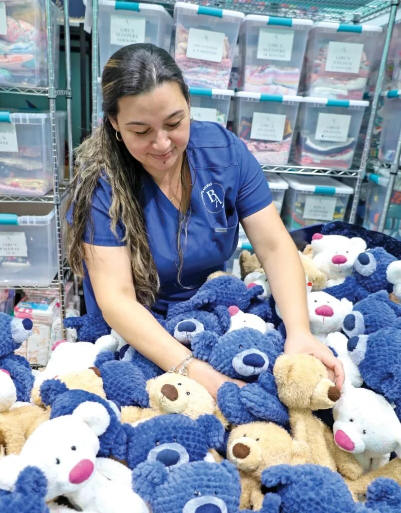 A woman in blue scrubs arranging teddy bears in a store.