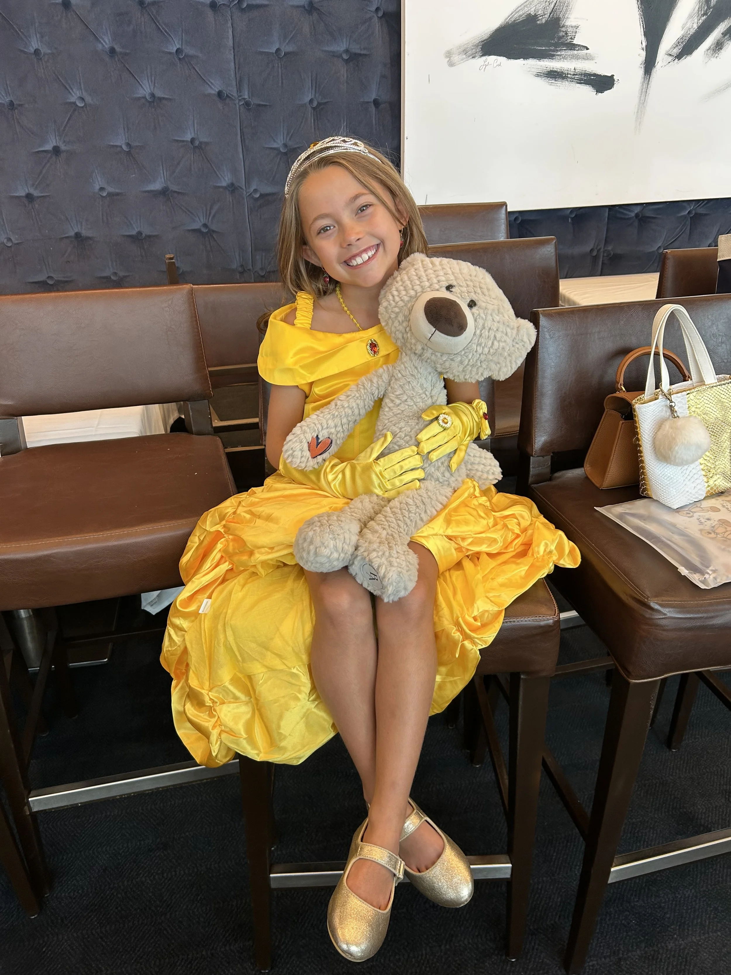 little girl wearing a princess dress smiling and holding benny bear