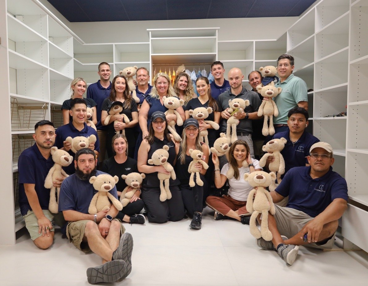 Group of people in a room holding teddy bears, with open shelves behind them.