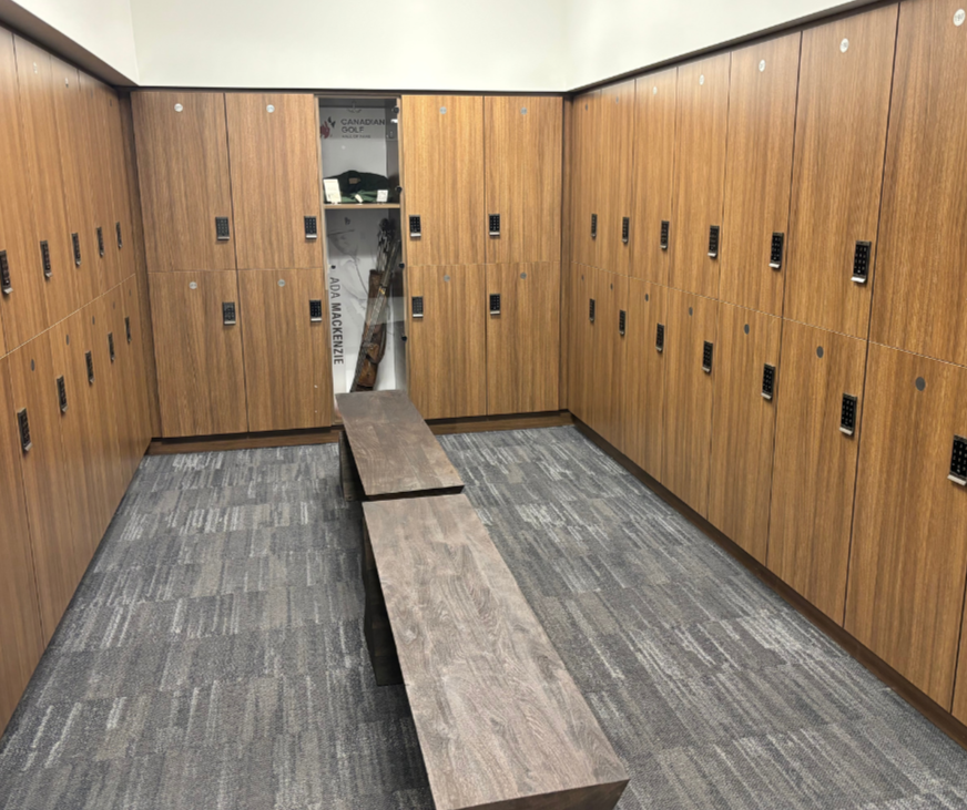 Golf locker room with lockers on three walls, a wooden bench in the centre, and a golf bag with clubs stored in a locker at the back.