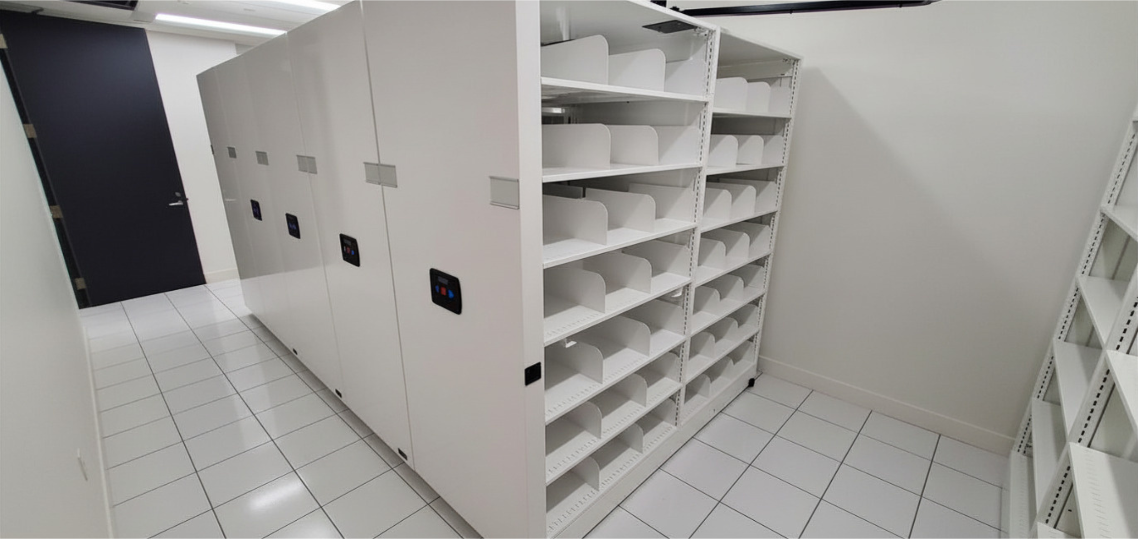 Empty white metal shelving unit with four shelves in a room with white and blue walls and a wood floor.