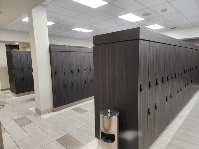 Row of black lockers in a gym or locker room with a trash can nearby.