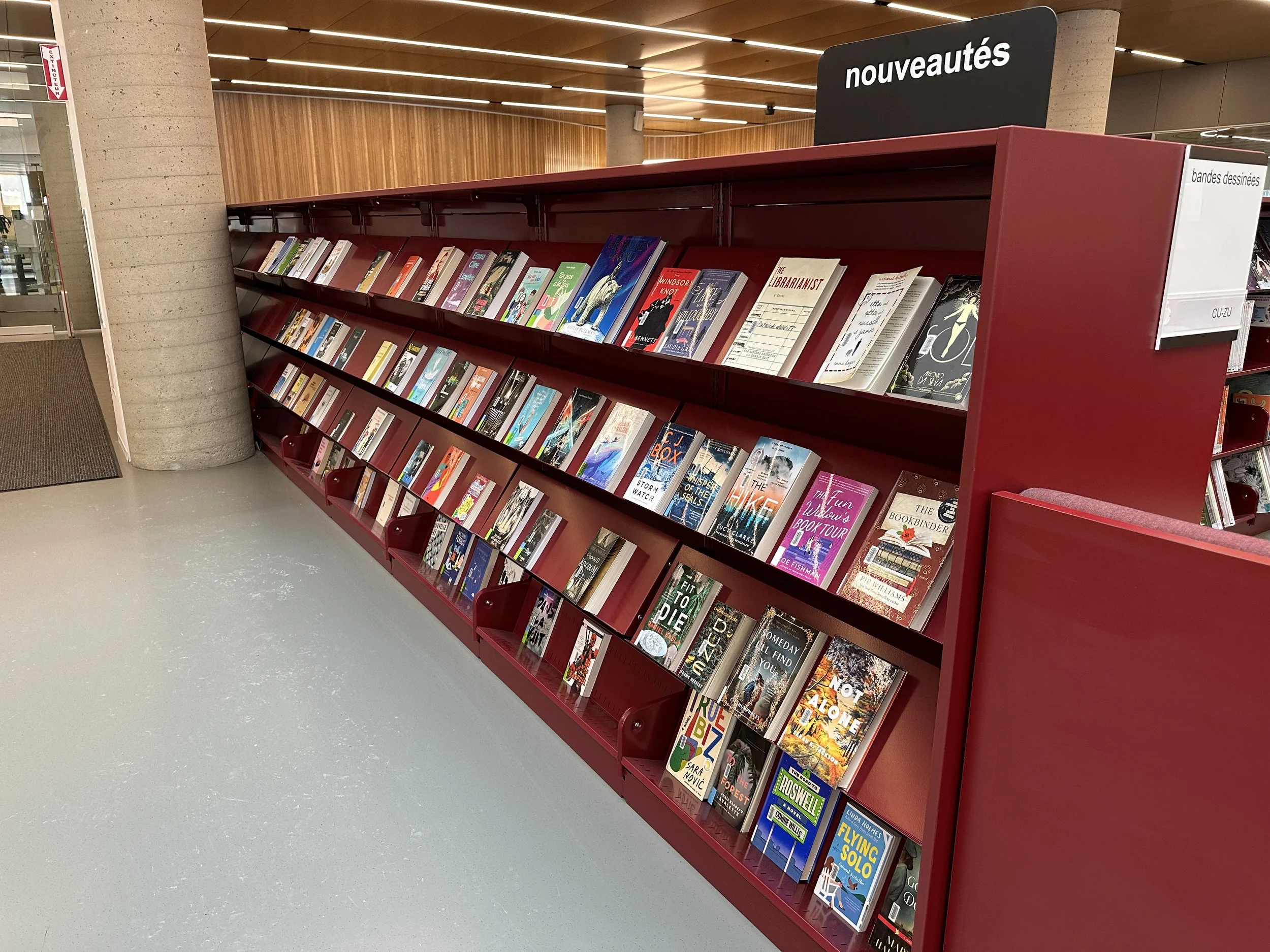 A person in a library sitting at a computer workstation with shelves of books in the background and modern green seating in the foreground.