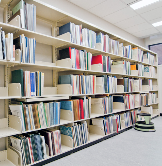 A person in a library sitting at a computer workstation with shelves of books in the background and modern green seating in the foreground.